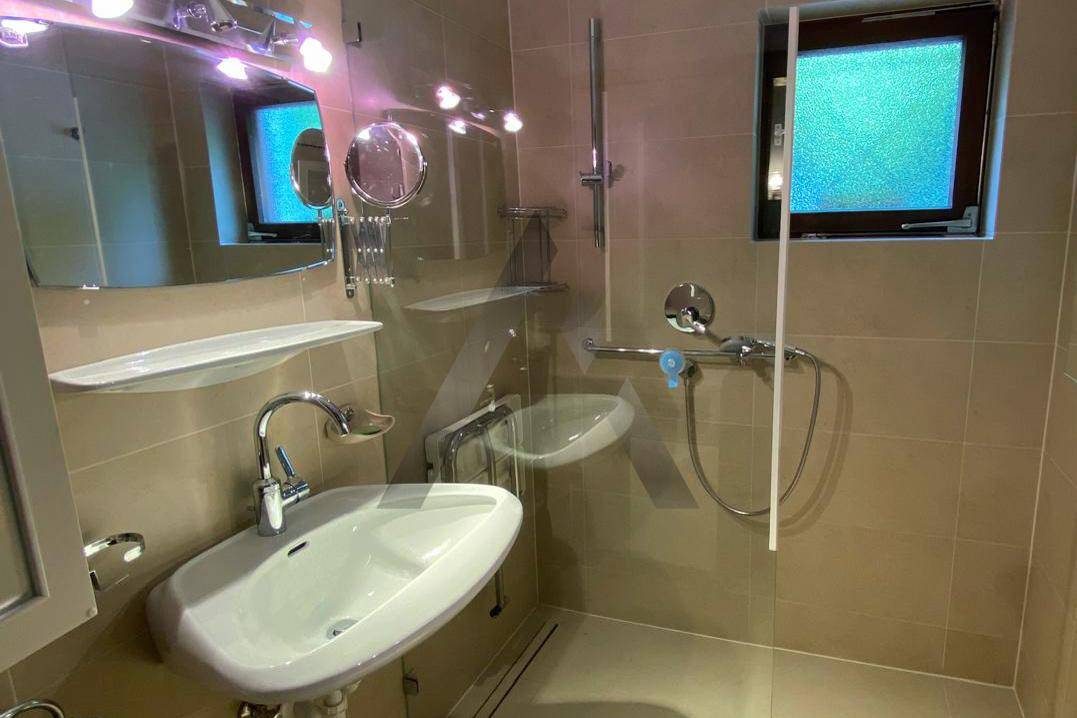Modernes Badezimmer mit beigefarbenen Fliesen, Dusche und Fenster.