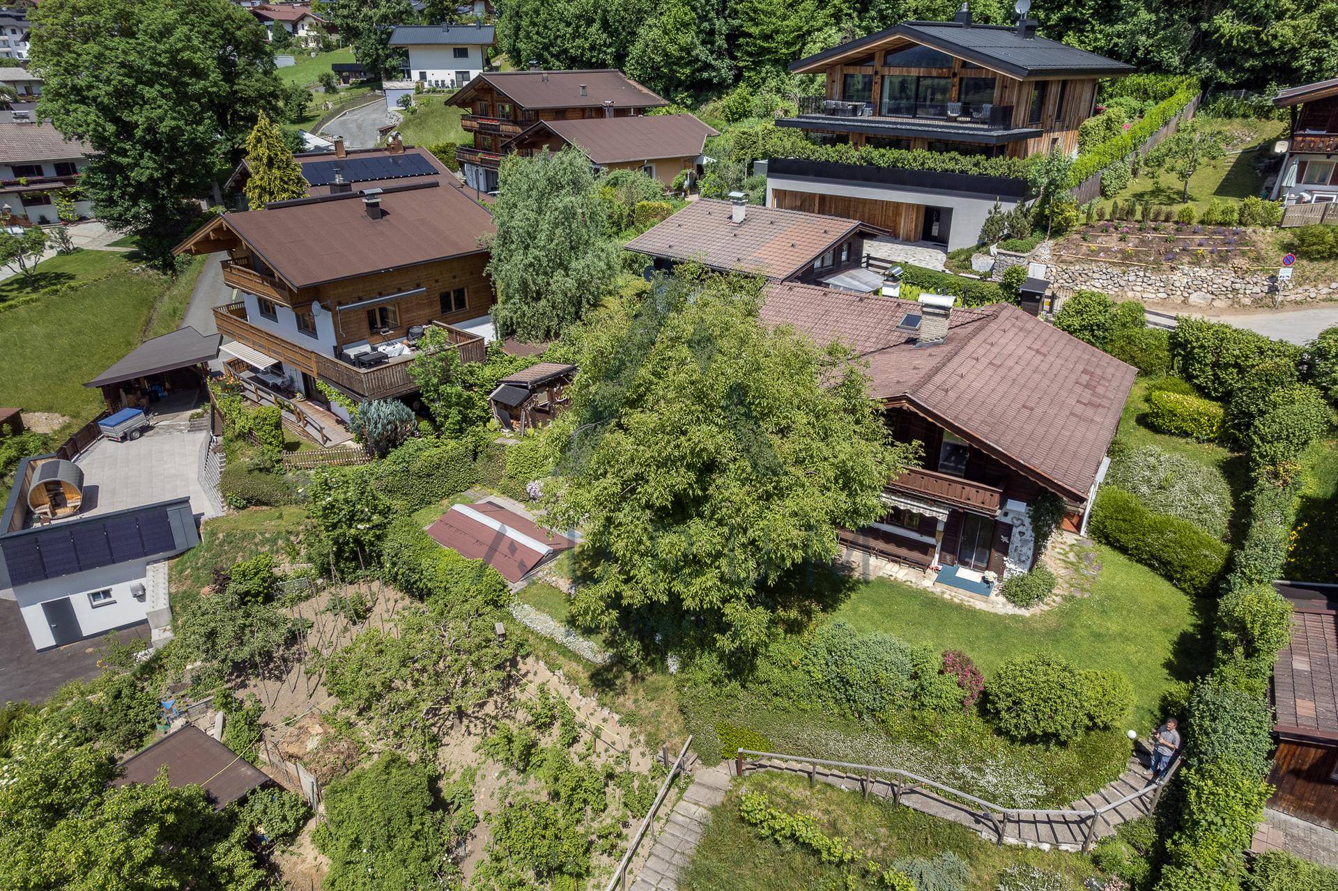 Panoramablick aus der Luft auf ein Wohngebiet mit Häusern, Gärten und einer bergigen Landschaft.