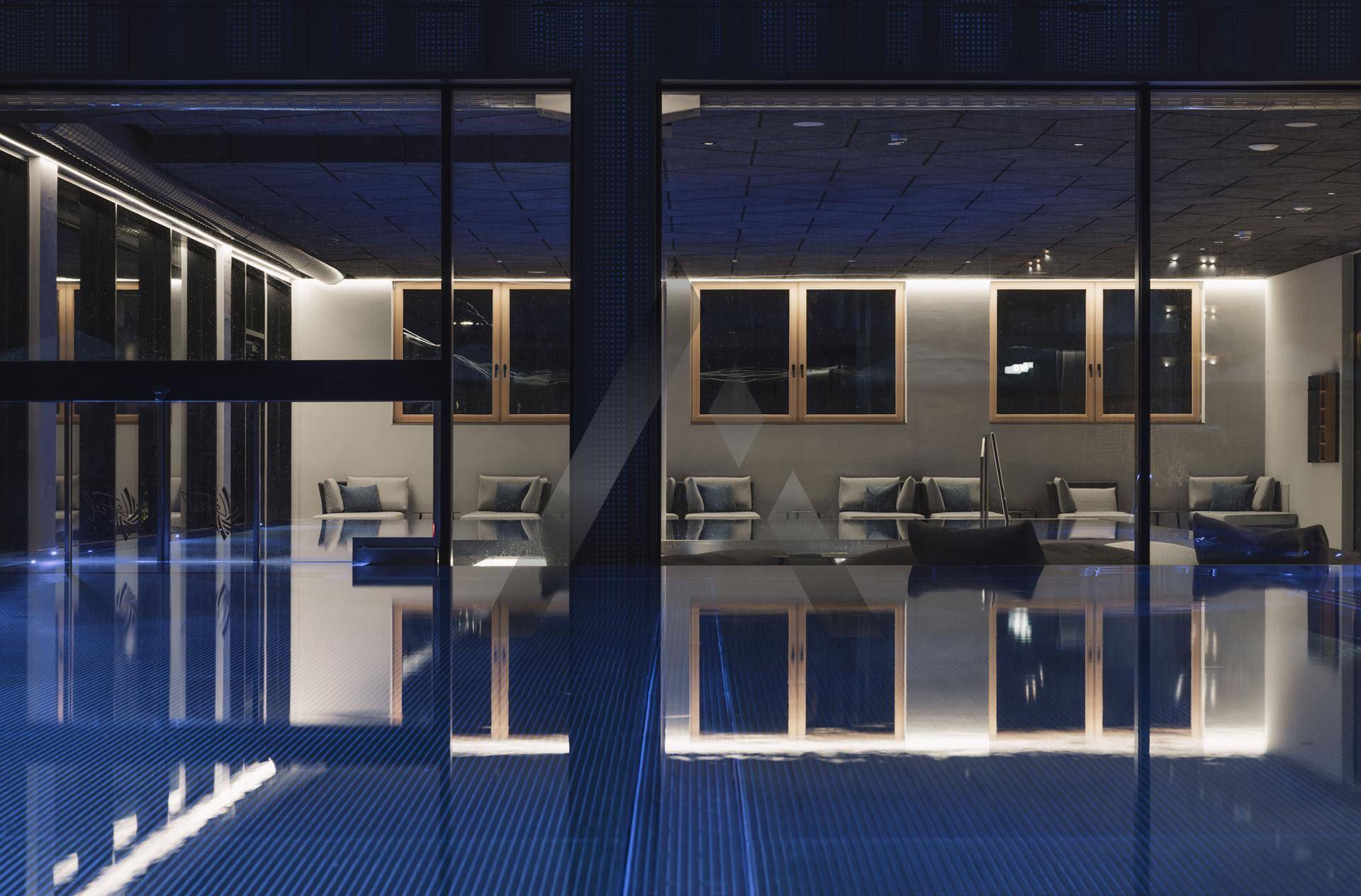 Innenpoolbereich bei Nacht mit reflektierenden Fenstern und stimmungsvoller Beleuchtung, die zum Entspannen einlädt.