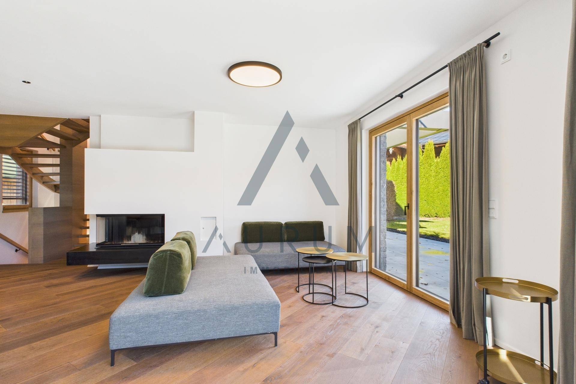 Helles Wohnzimmer mit modernem Kamin, Holzboden und Zugang zum Garten durch große Glasfronten.