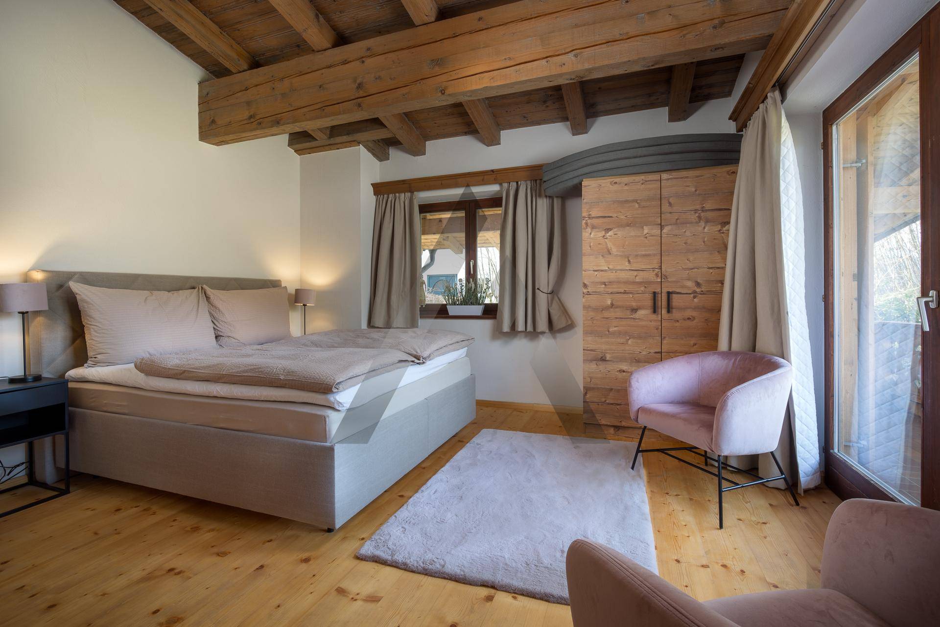 Geräumiges Schlafzimmer mit Holzboden, sichtbaren Balken und Balkonzugang für frische Luft.