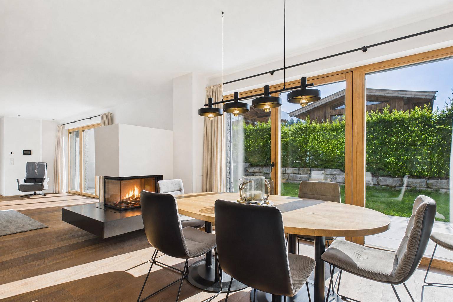 Essbereich mit Holztisch, modernen Stühlen und großen Fenstern mit Blick auf den grünen Garten.