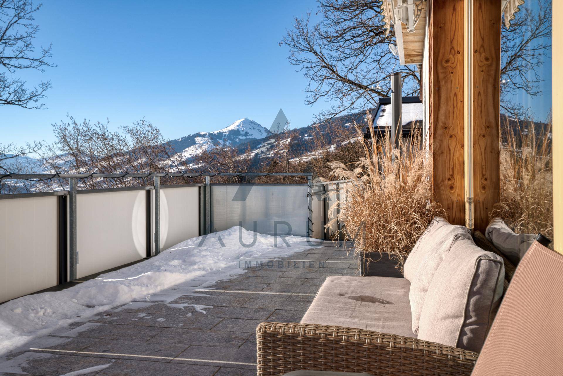 Gemütliche Terrasse mit Outdoor-Sitzgelegenheiten, umgeben von Schnee und mit Blick auf die Berge.