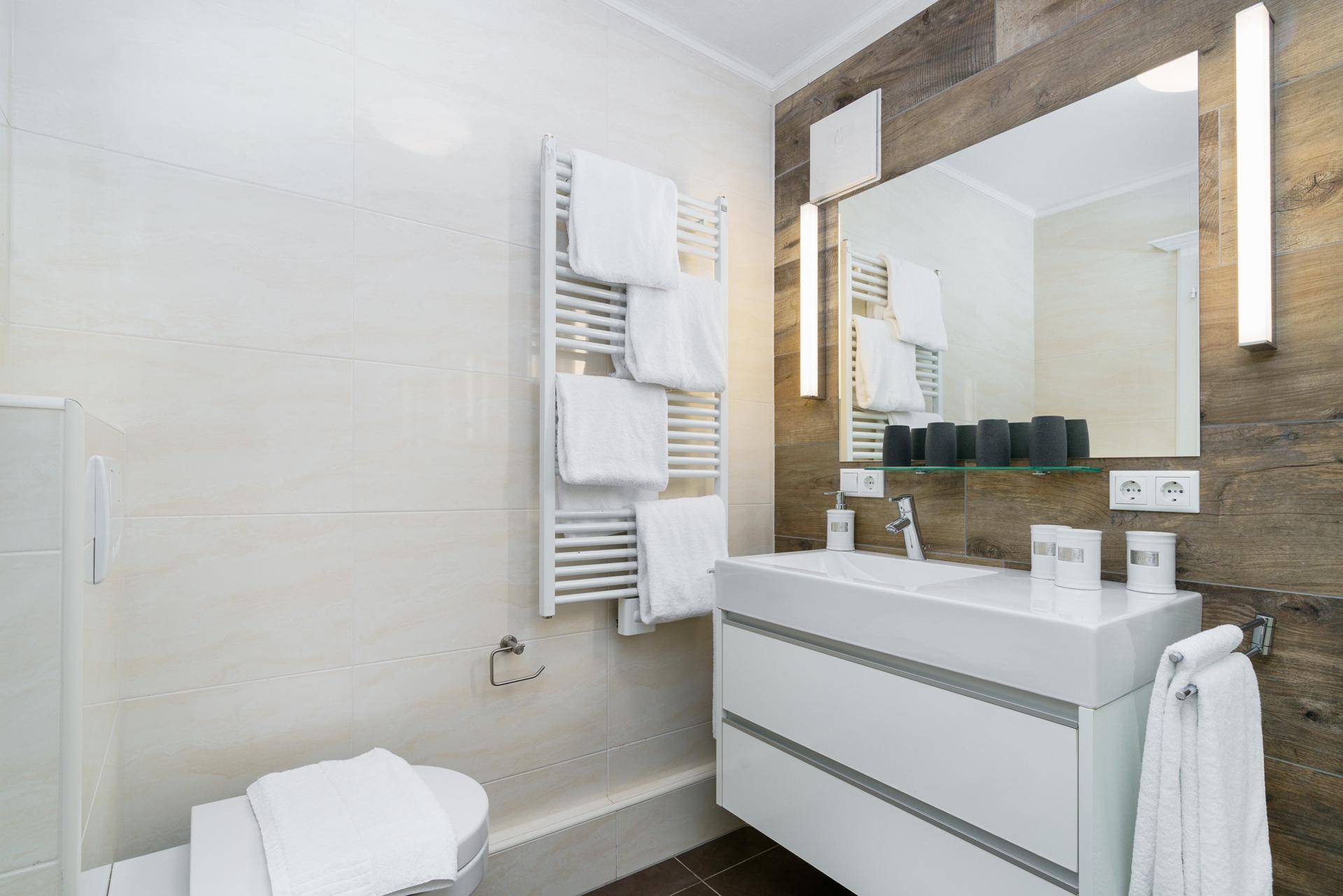 Modernes Badezimmer mit Waschtisch, Wand-WC und beheiztem Handtuchhalter, kombiniert mit Holz- und Fliesenakzenten.