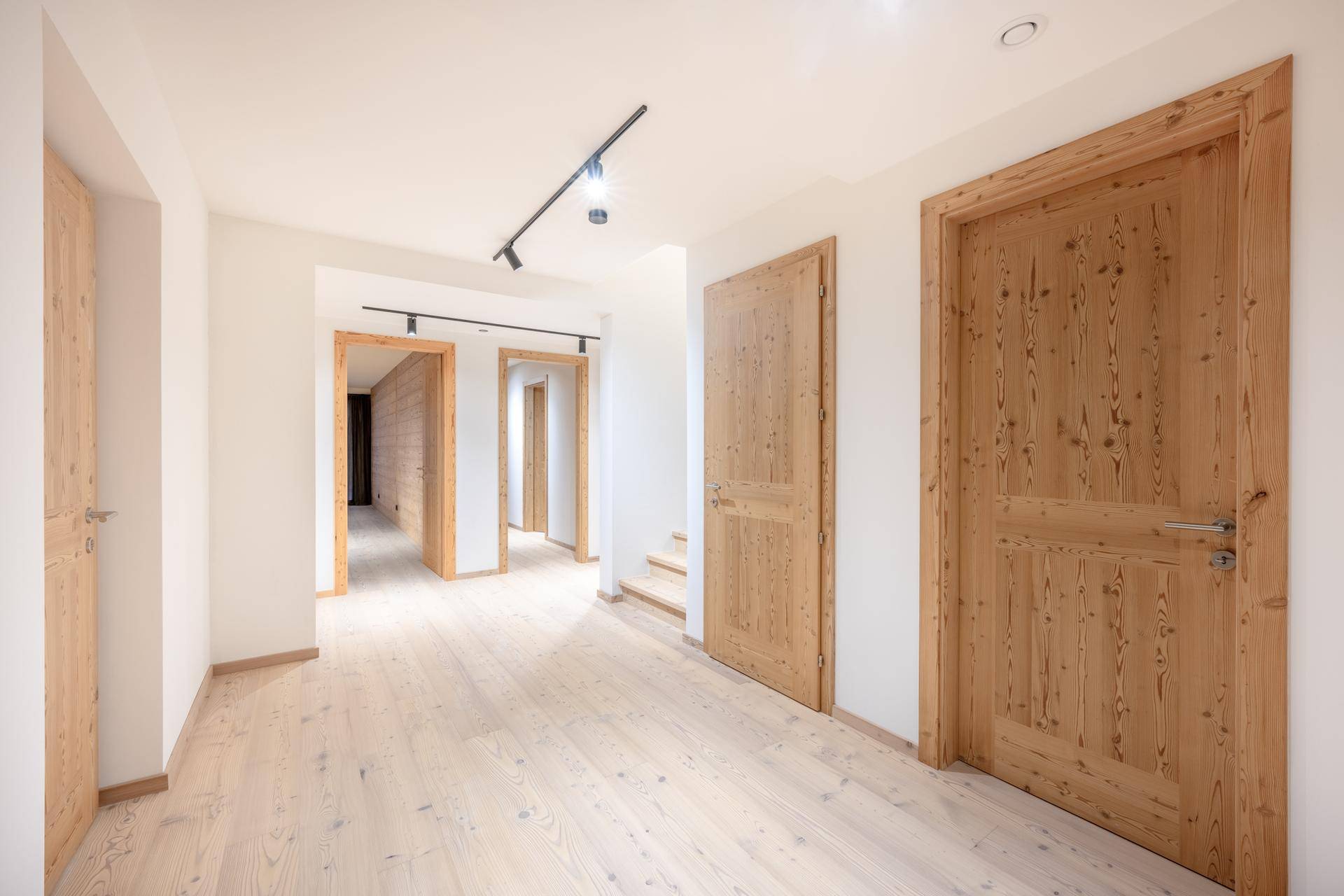 Heller Flur mit Holztüren, Holzboden und minimalistischer Beleuchtung.