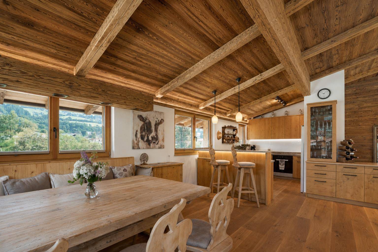Rustikaler Essbereich mit Holztisch und Blick auf die offene Küche im alpinen Design.