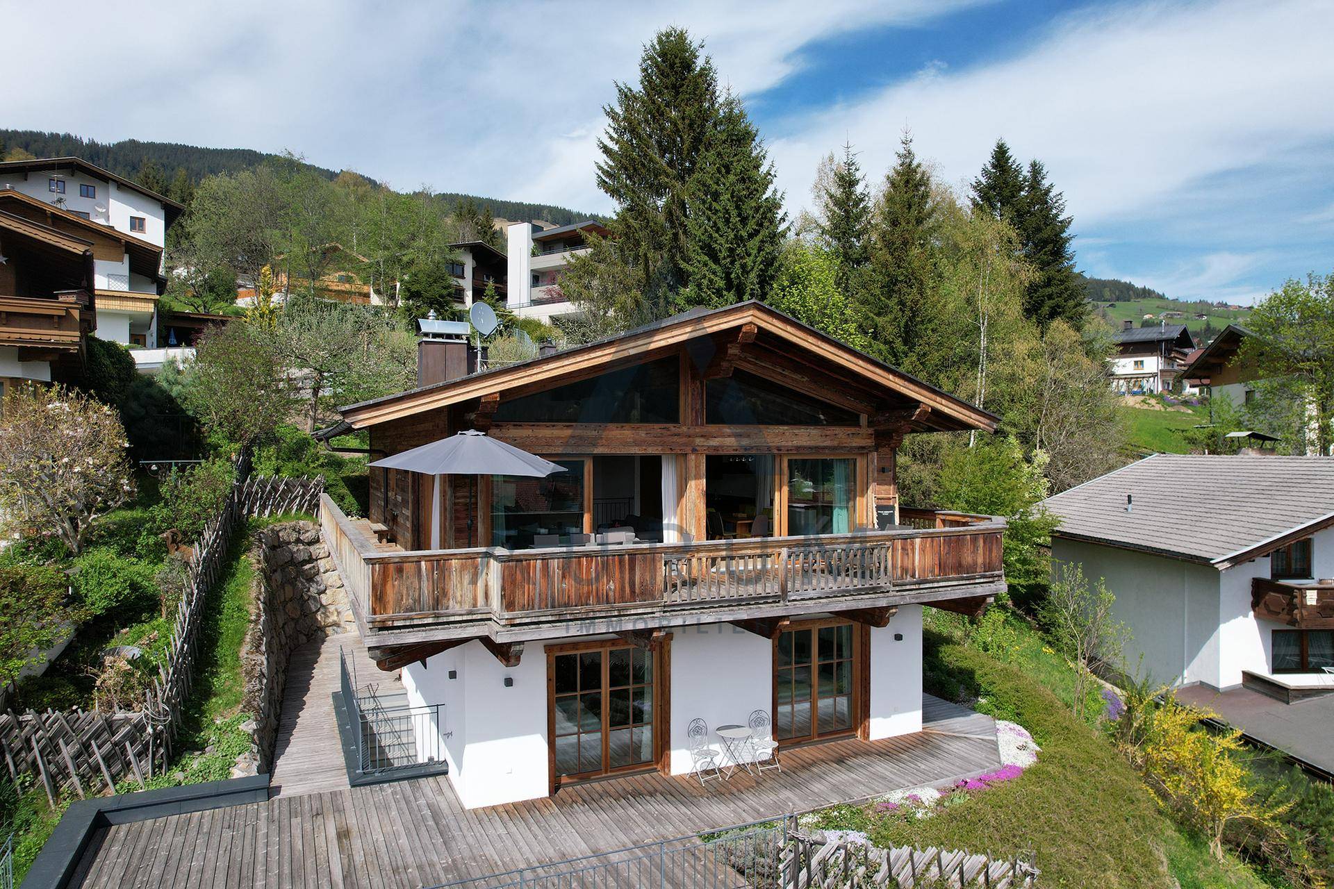 Chalet-Anwesen in Hanglage mit Balkon und Terrasse, umgeben von grüner Natur und Bergen.