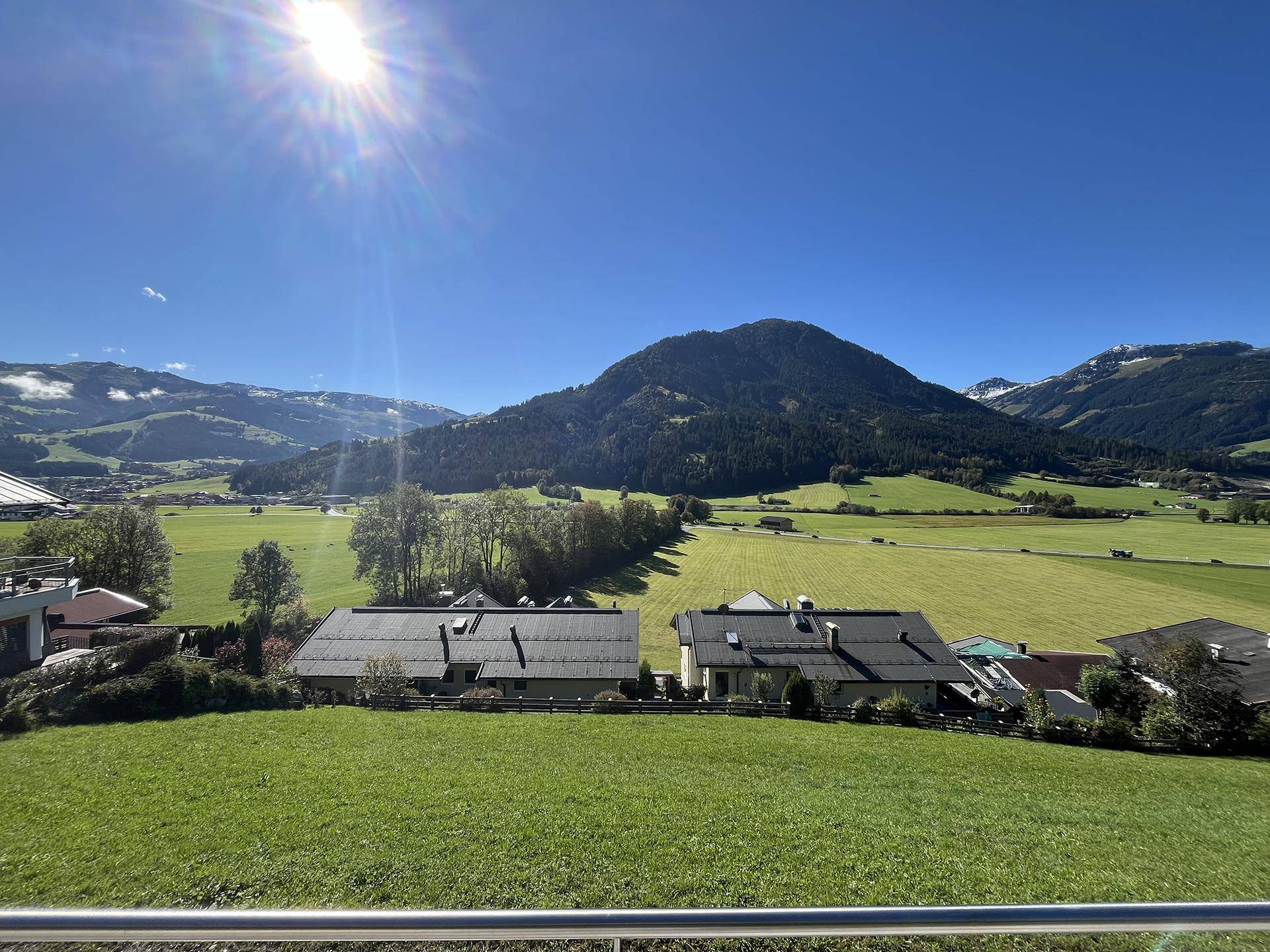 Sonniger Ausblick auf die umliegende Berglandschaft mit weiten grünen Wiesen und vereinzelten Häusern.