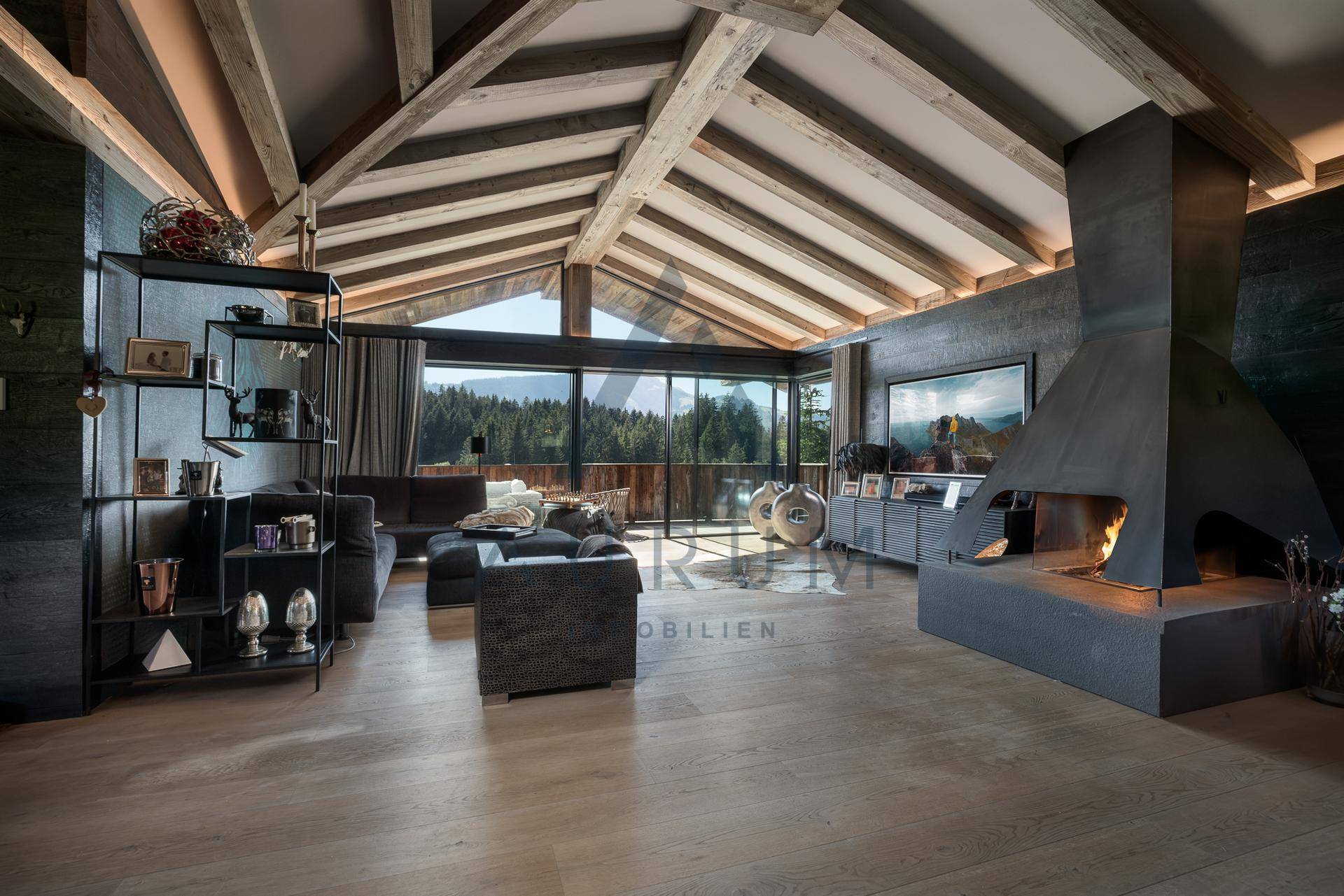 Großzügiges Wohnzimmer mit Holzbalkendecke, Kamin und bodentiefen Fenstern mit Bergblick.