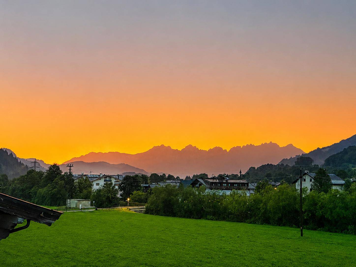 Atemberaubender Sonnenuntergang über der Berglandschaft mit grünen Wiesen im Vordergrund.