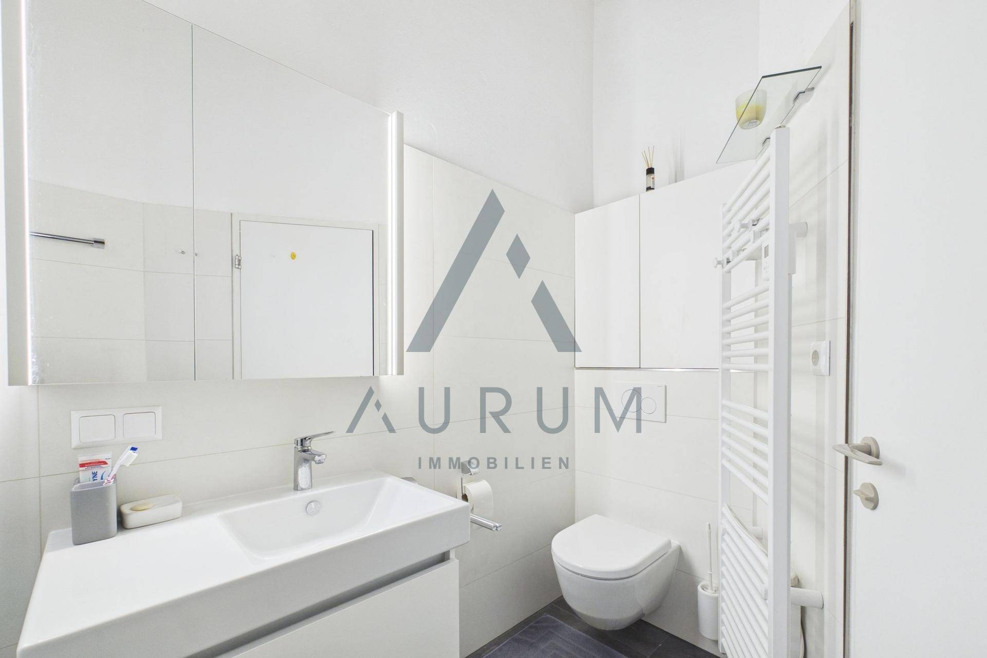 Helles Badezimmer mit WC, Waschbecken, beheiztem Handtuchhalter und Spiegelschrank.