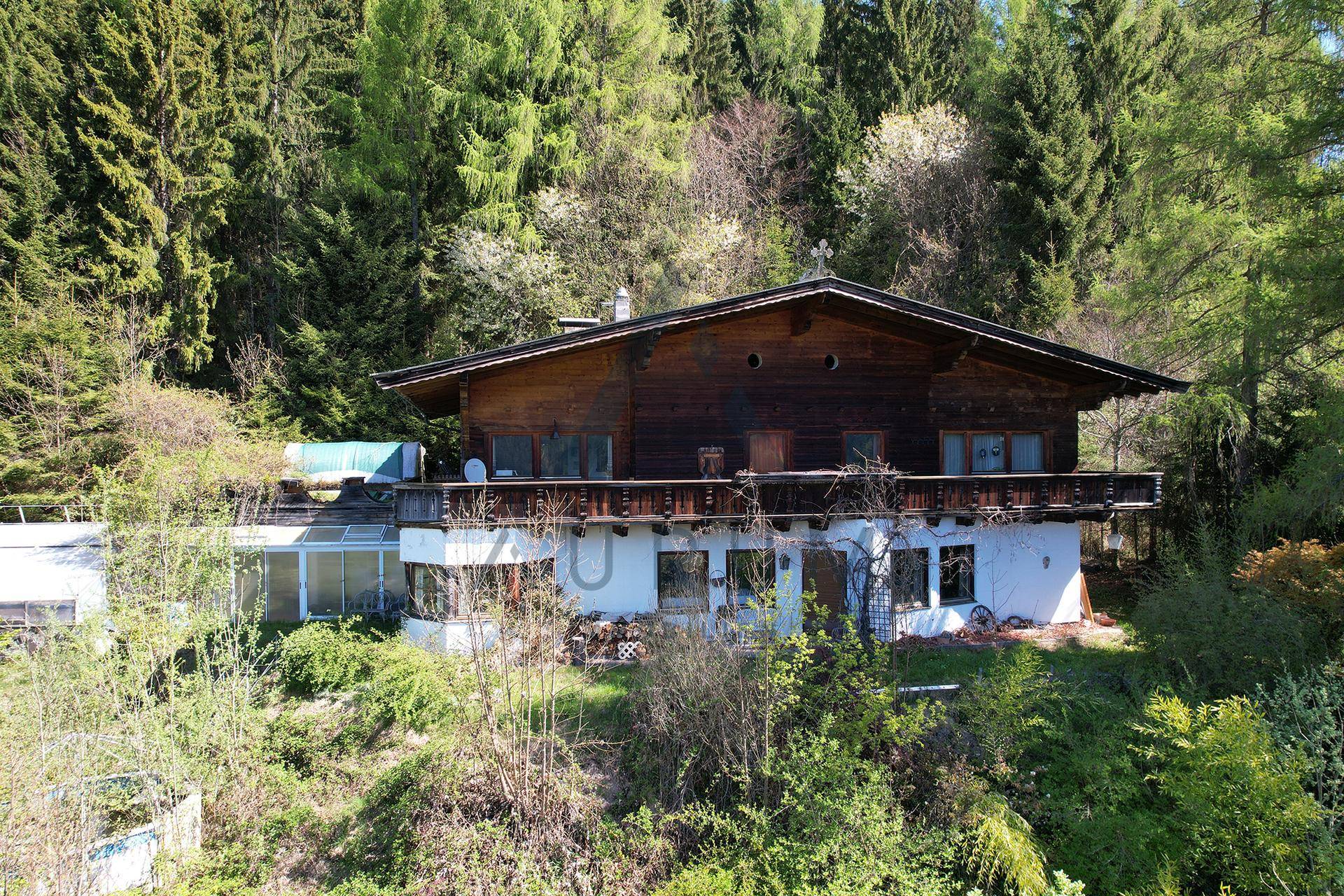 Traditionelles Holzchalet mit Balkonen und einem Wintergarten, eingebettet in grüne Natur.
