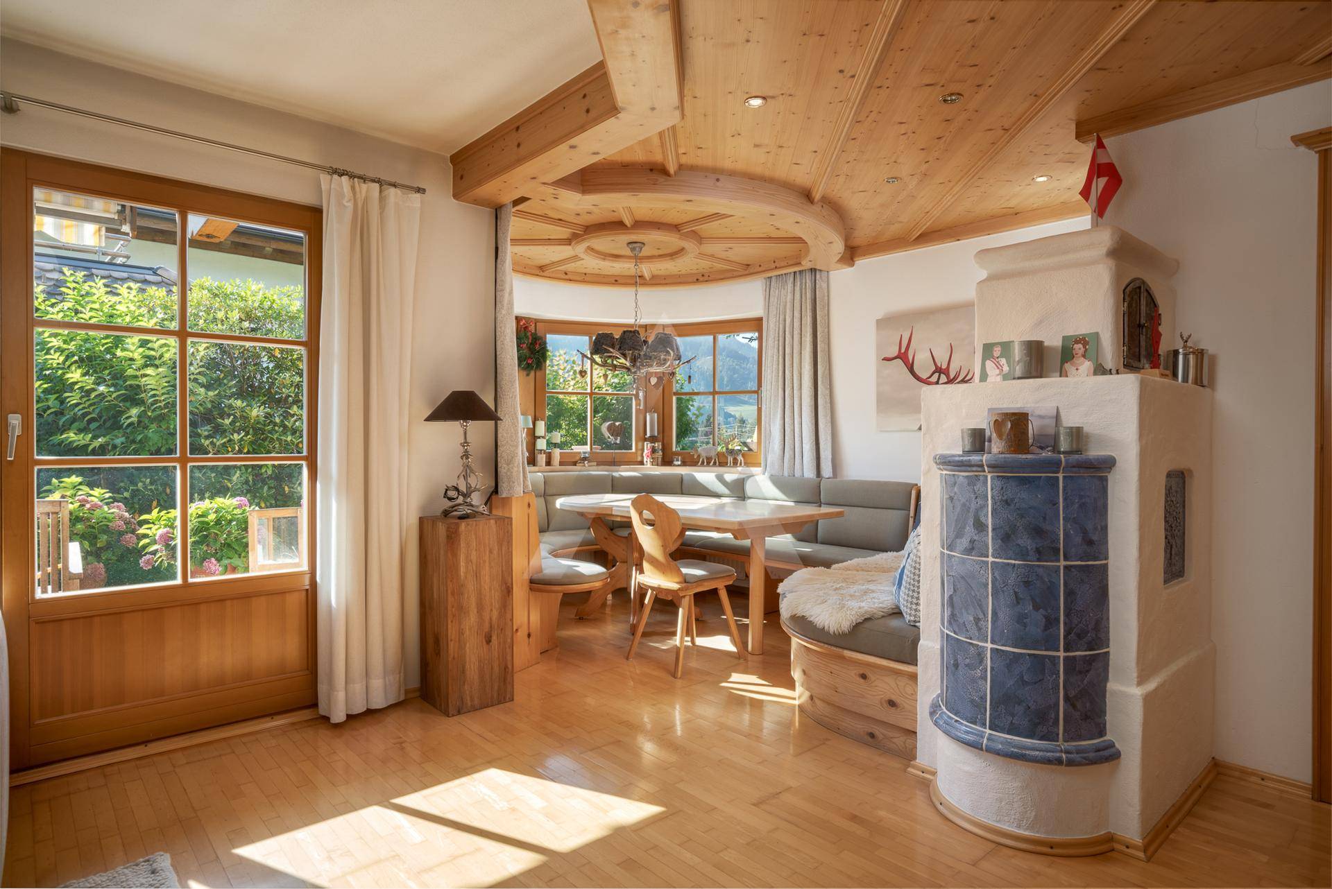 Gemütlicher Essbereich im alpinen Stil mit Kachelofen, Holzbalkendecke und Blick ins Grüne.