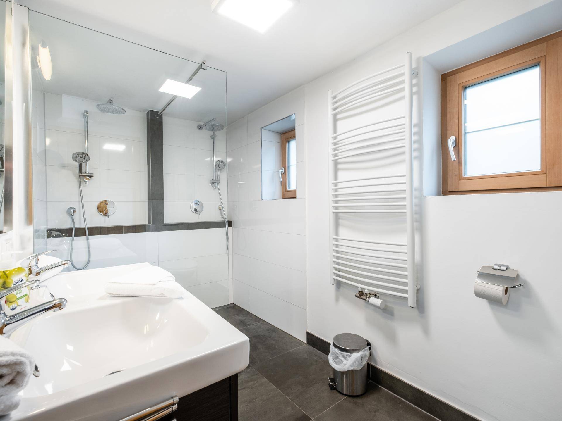Modernes Badezimmer mit ebenerdiger Dusche, Einzelwaschbecken, WC und beheiztem Handtuchhalter.