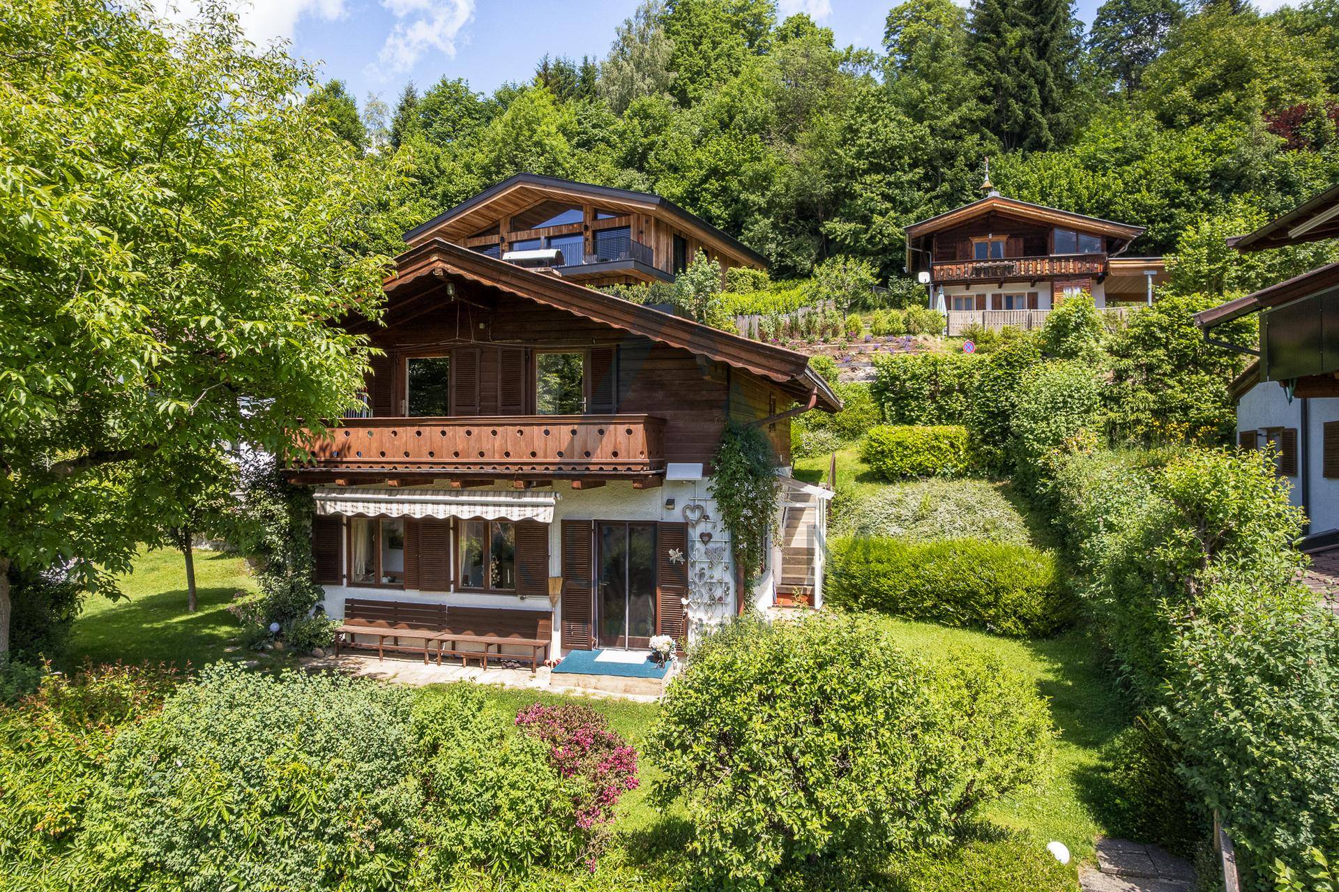 Charmantes Holzhaus mit Balkon und grüner Umgebung, eingebettet in eine hügelige Landschaft.