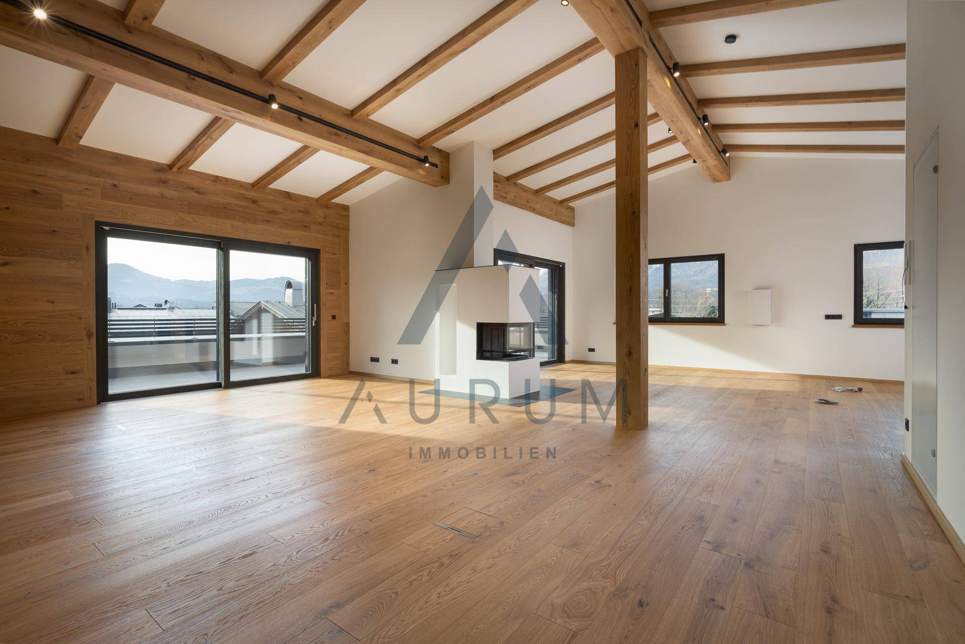 Geräumiges Wohnzimmer mit Holzbalken, Kamin und Zugang zu einer großen Terrasse mit Bergblick.