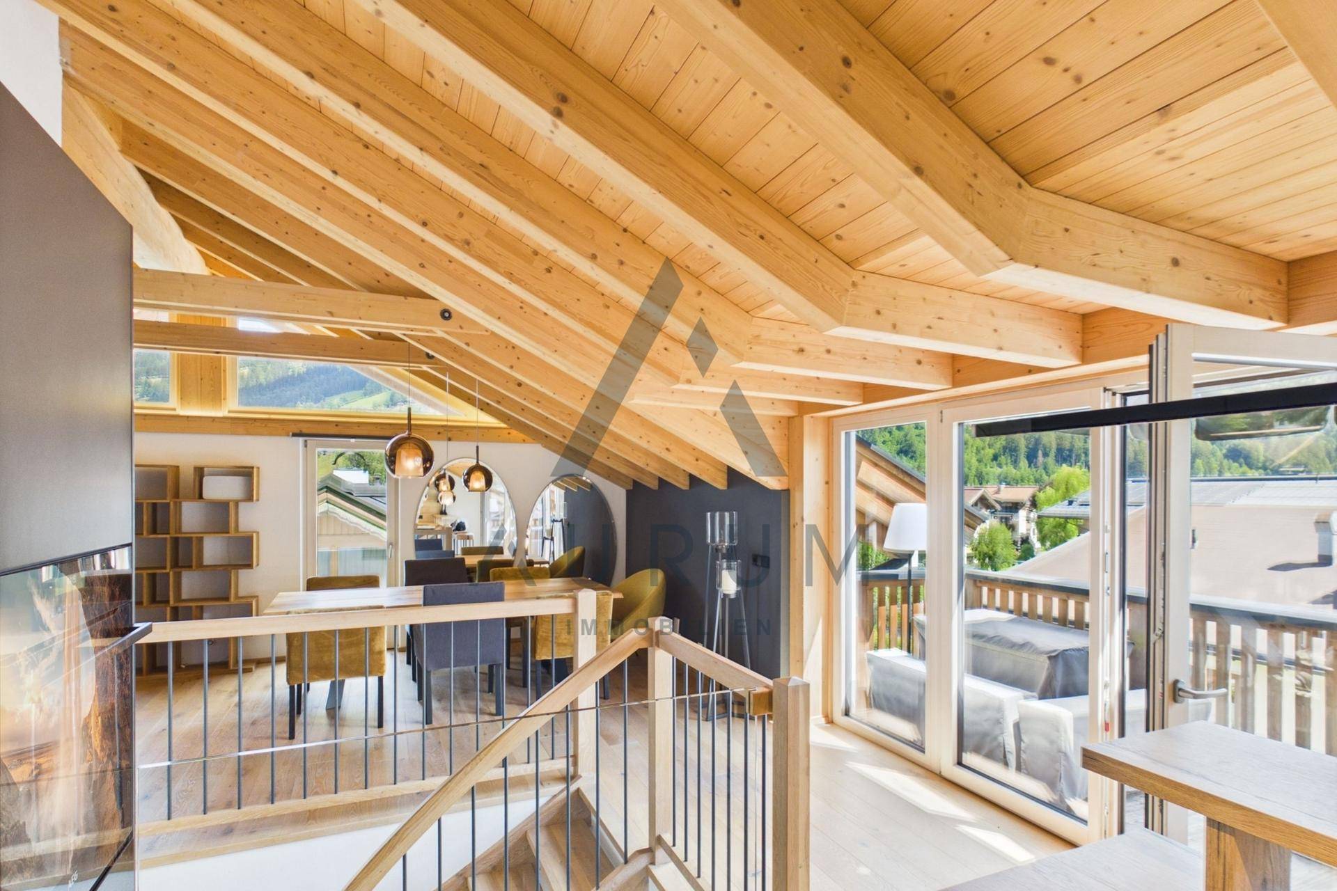 Geräumiger offener Wohn- und Essbereich mit Holzbalken, Kamin und Zugang zum Balkon.