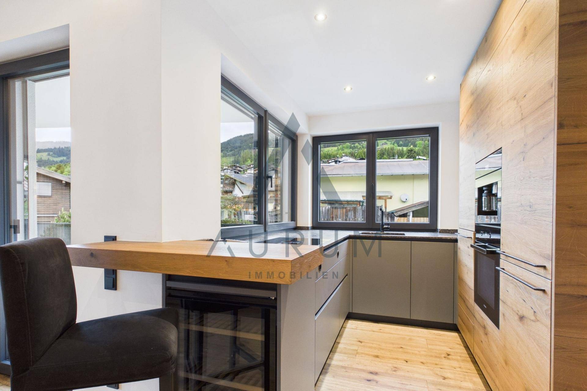 Moderne Küche mit Holzelementen, dunkler Arbeitsplatte und integriertem Frühstücksbereich mit Bergblick.