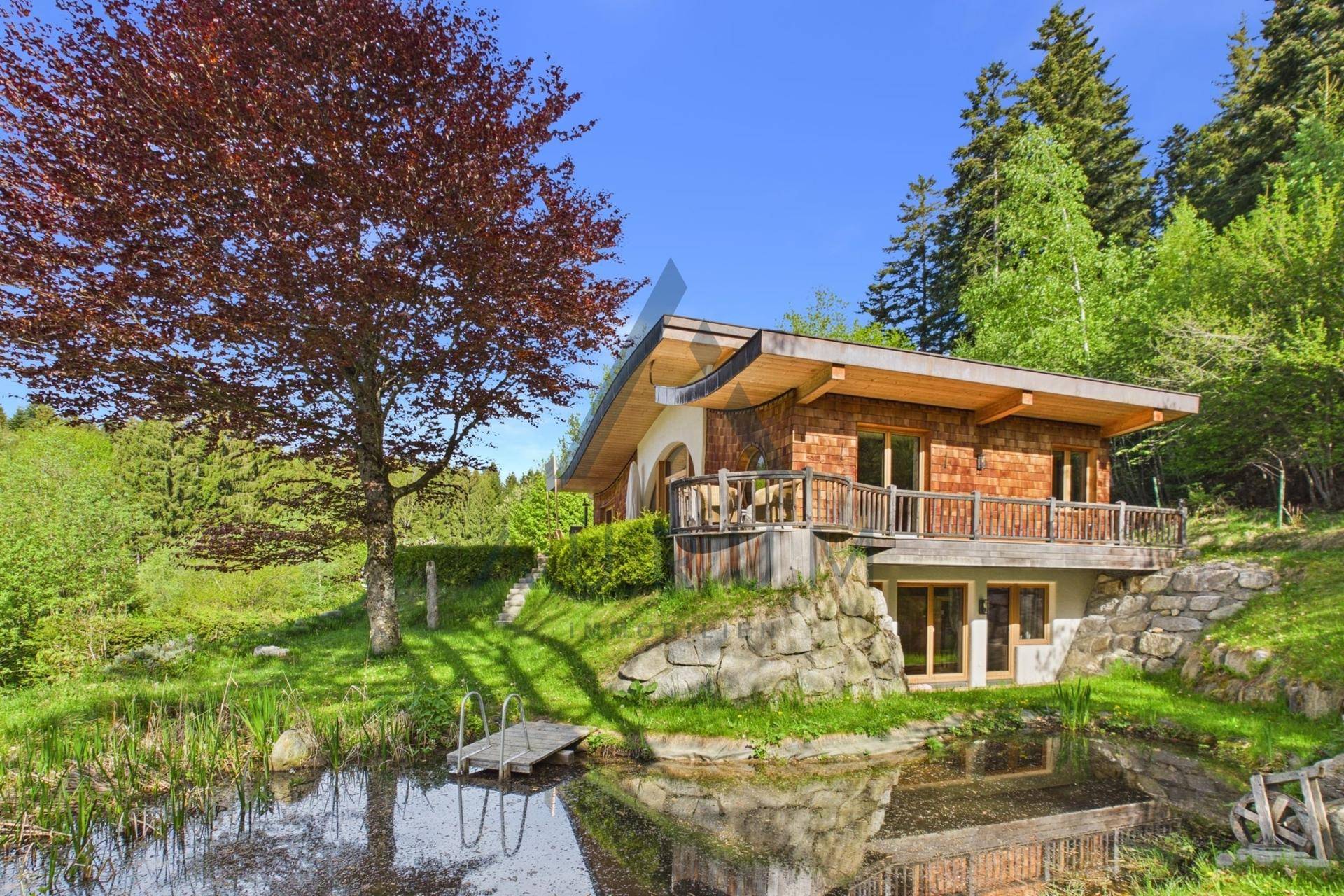 Idyllisches Holzhaus am Teich mit kleinem Steg, umgeben von üppiger Natur.