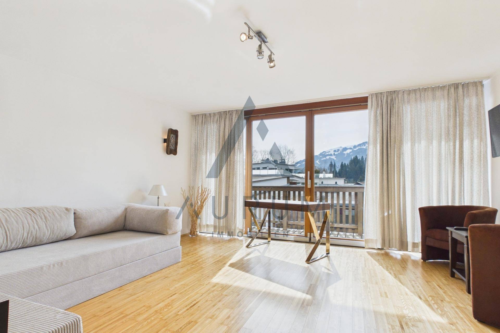 Lichtdurchflutetes Wohnzimmer mit Holzboden, Balkonzugang und Bergblick.