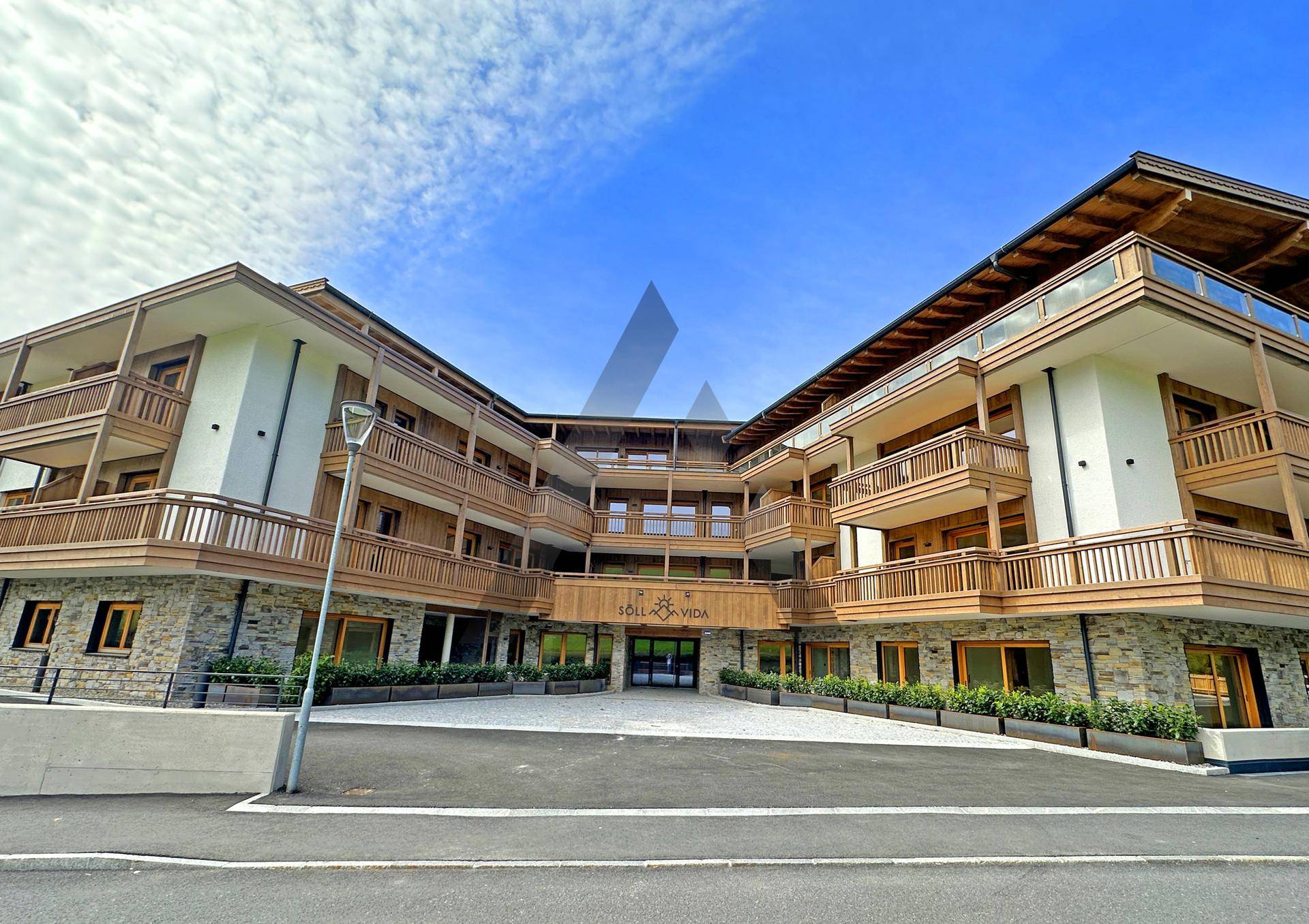 Elegante Fassade eines modernen Gebäudes im alpinen Stil mit vielen Balkonen und Steinverkleidung.