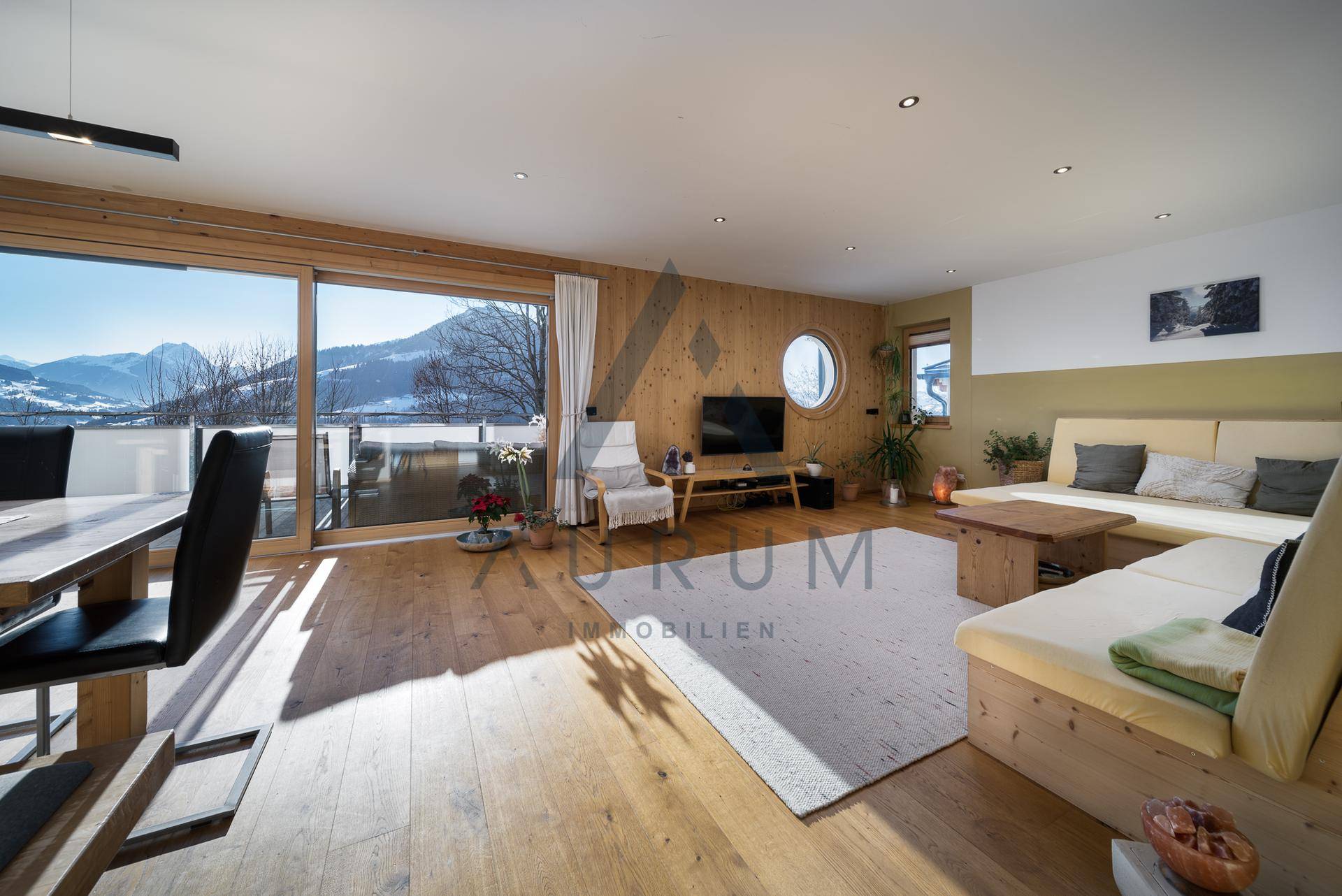 Gemütlicher Wohnbereich mit Holzboden, bequemen Sofas und weitem Blick auf die verschneiten Berge.