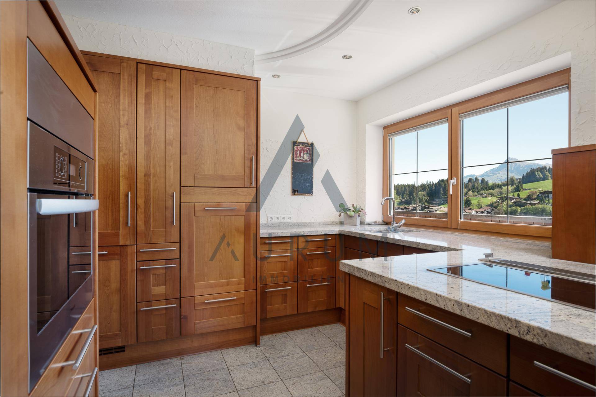 Gemütliche Holzküche mit Granitarbeitsplatten, Einbaugeräten und einem Fenster mit Bergblick.