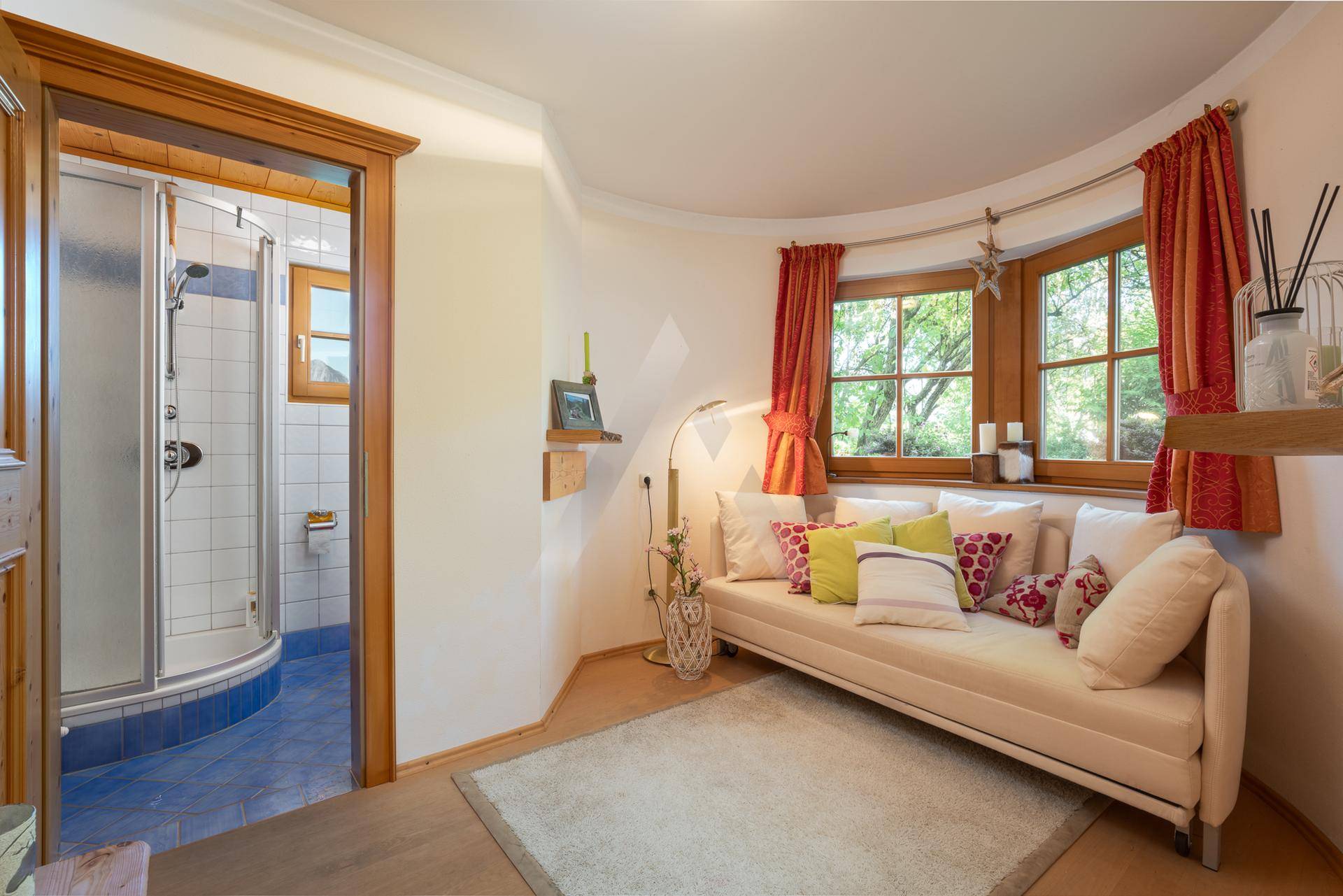 Helles Schlafzimmer mit Tagesbett, bunten Kissen und angrenzendem Duschbad.