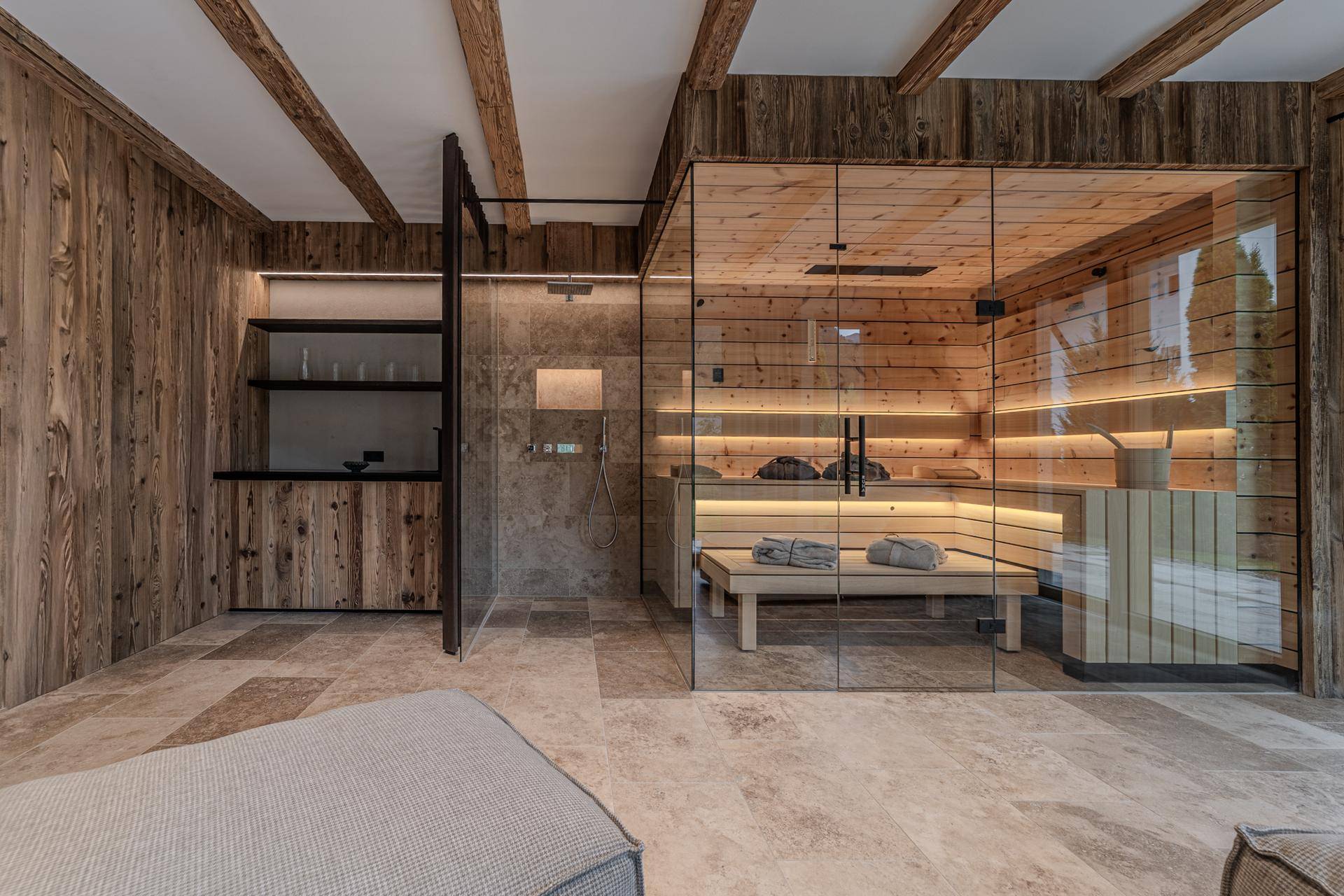 Moderner Wellnessbereich mit Glas-Sauna, Dusche und Blick ins Grüne durch große Fenster.