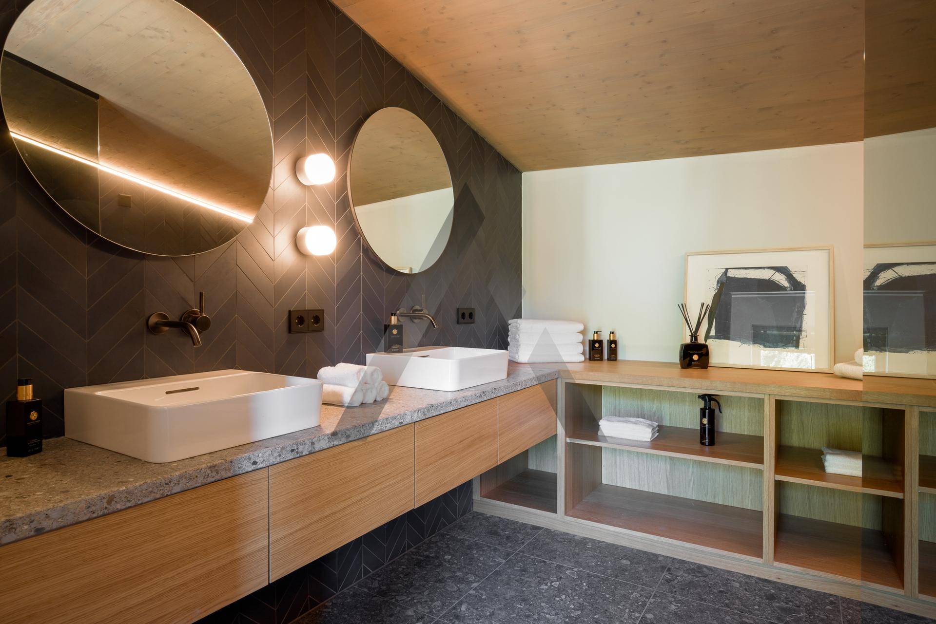 Modernes Badezimmer mit Doppelwaschbecken, runden Spiegeln und dunklen Fliesenwänden.