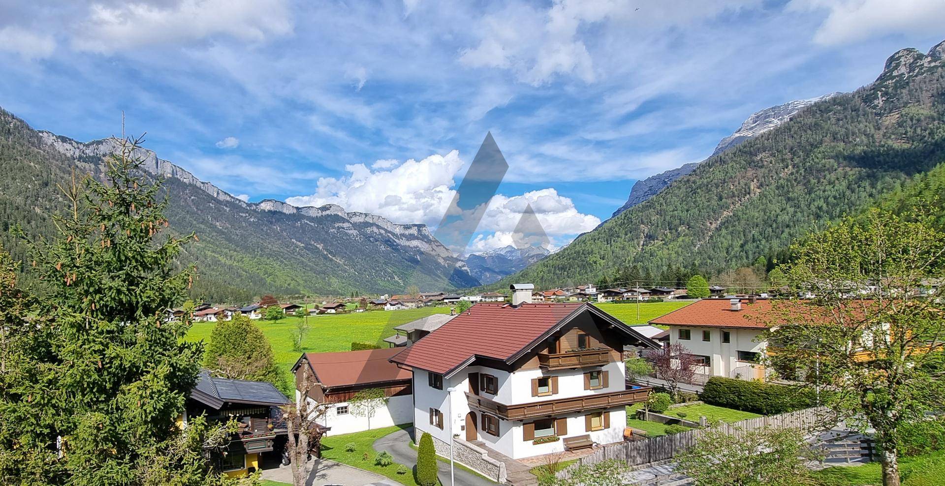 Weitläufiger Blick über das Tal mit traditionellen Häusern, grünen Wiesen und majestätischen Bergen.