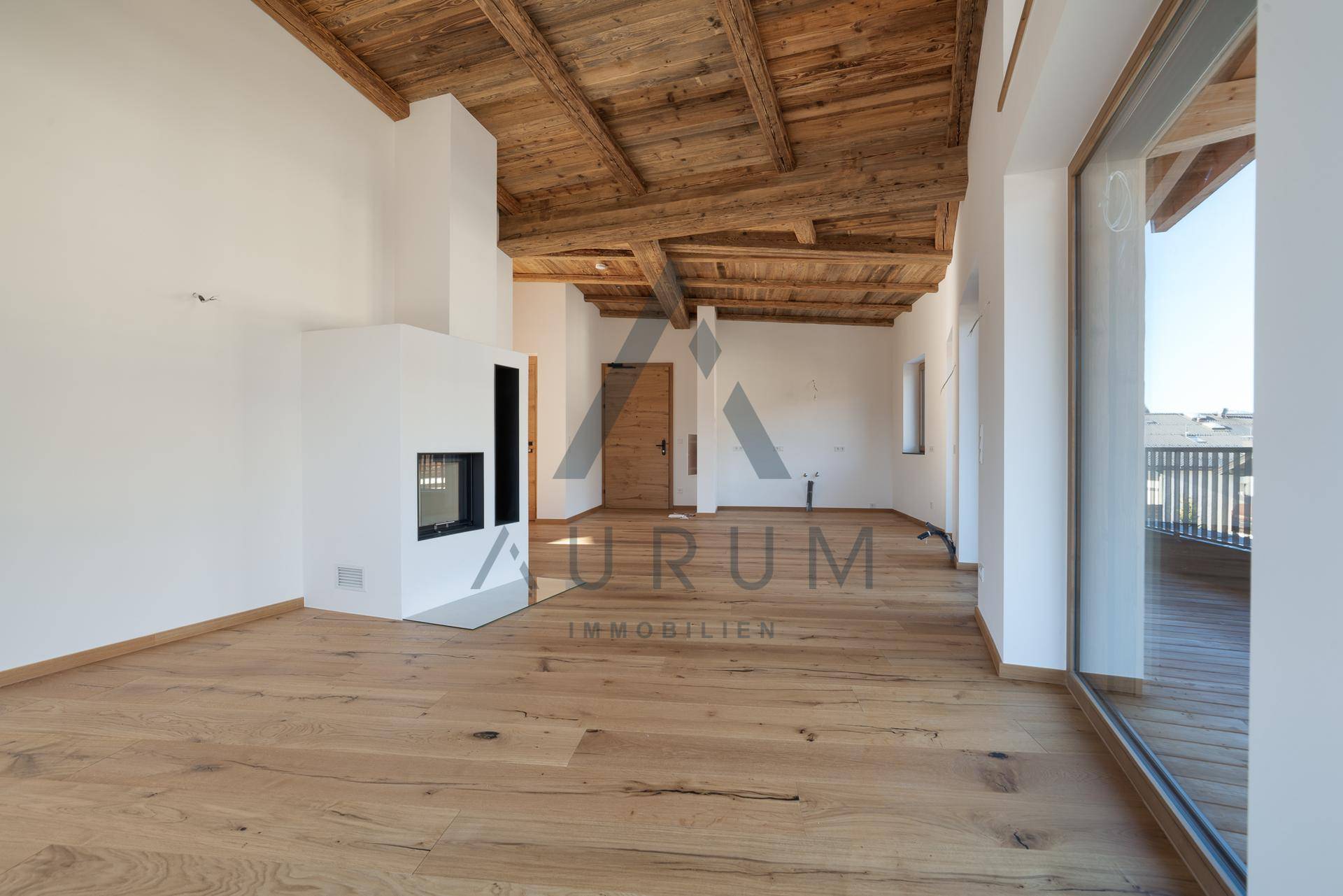 Geräumiger Wohnbereich mit Holzboden, sichtbarer Holzdecke und einem modernen Kamin.