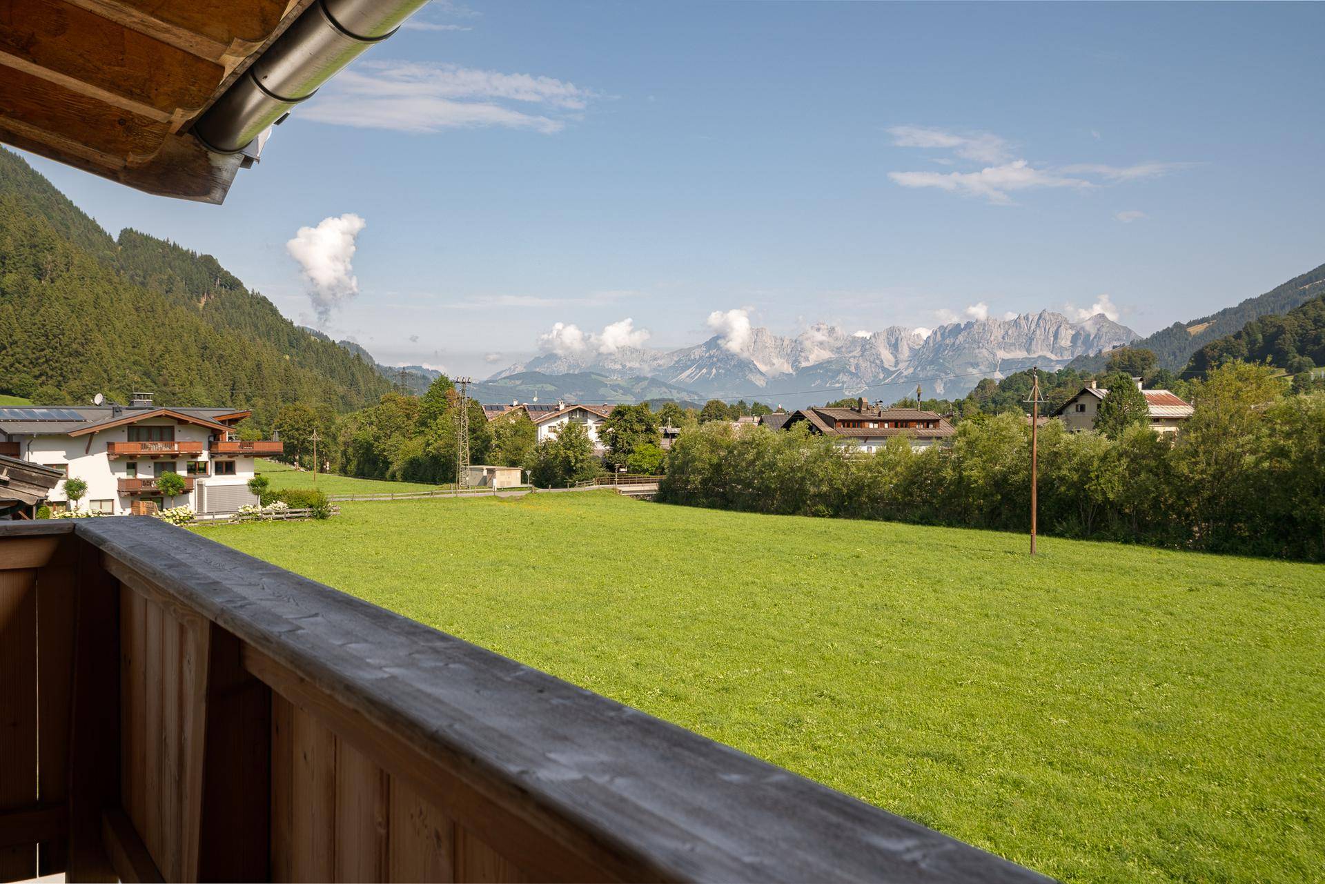 Malerischer Ausblick vom Balkon auf grüne Wiesen und die majestätische Bergwelt.