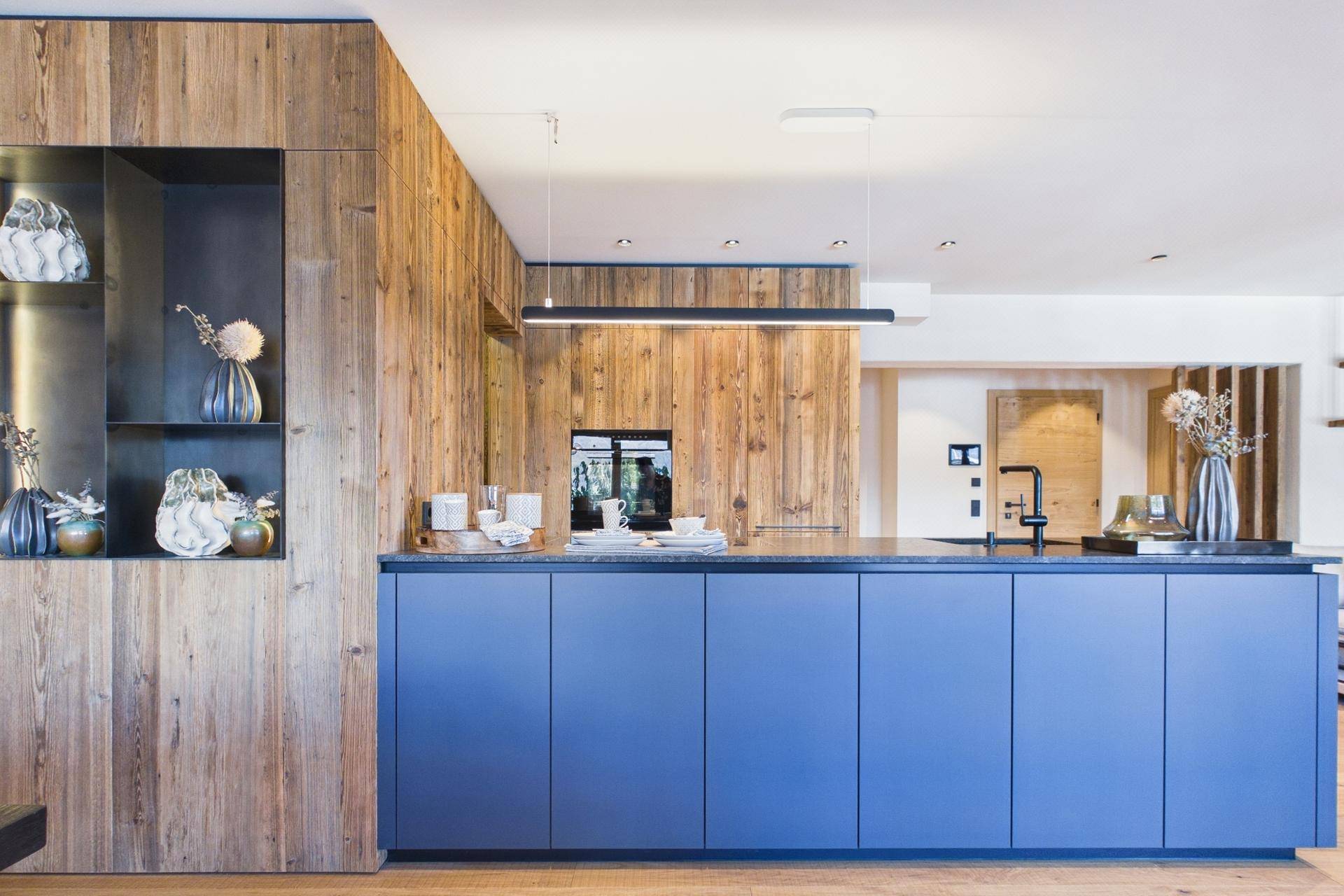 Moderne Küche mit blauen Unterschränken, Holzverkleidung und integrierten Geräten.