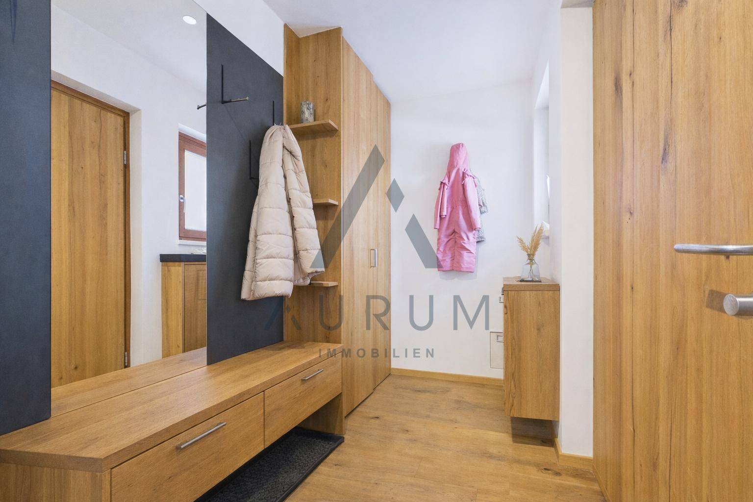Heller Eingangsbereich mit Holzeinbauten, Garderobe und großem Spiegel für praktische Nutzung.