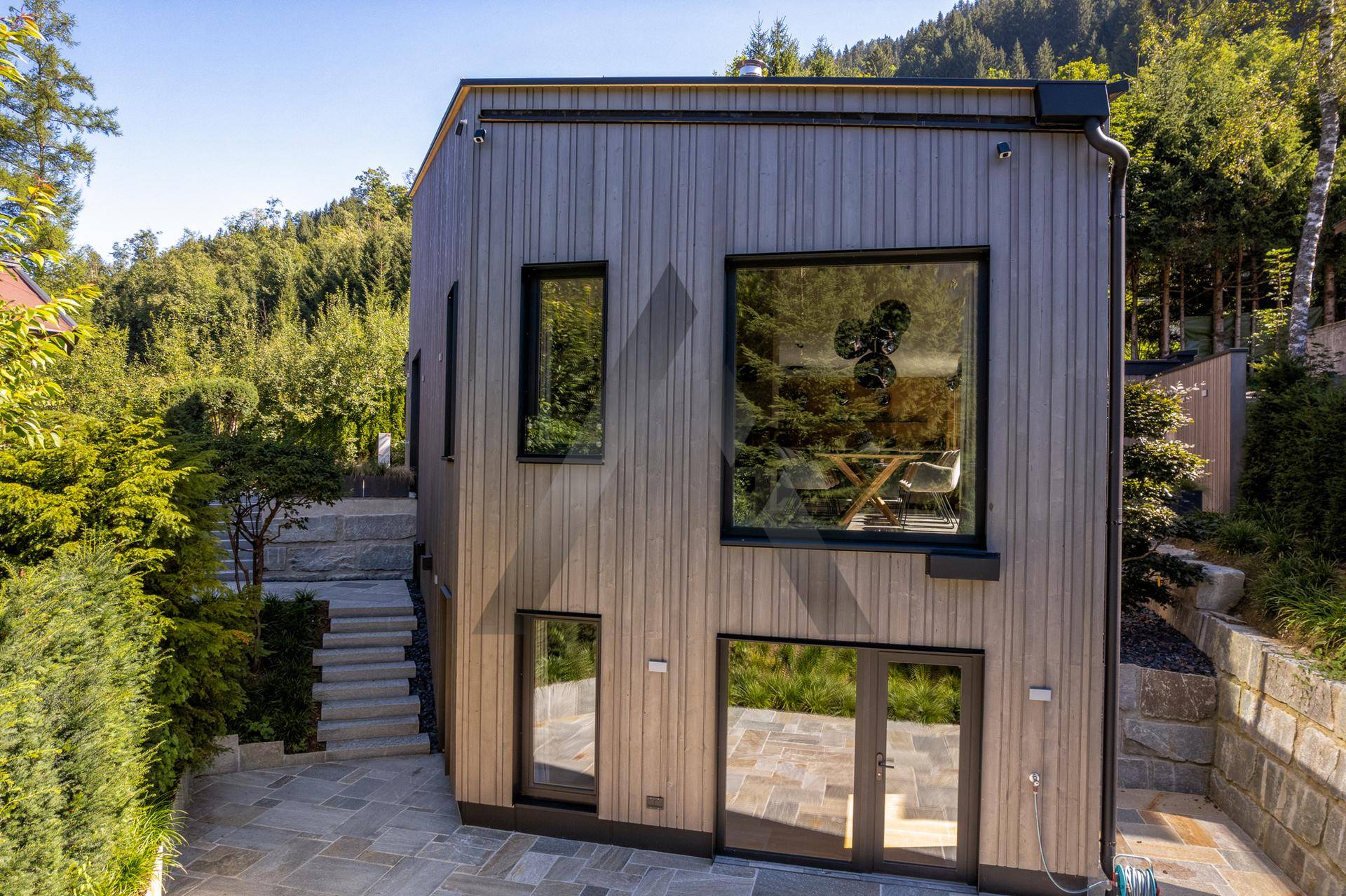 Ansicht der modernen Holzfassade mit großen Fenstern und gepflastertem Außenbereich.