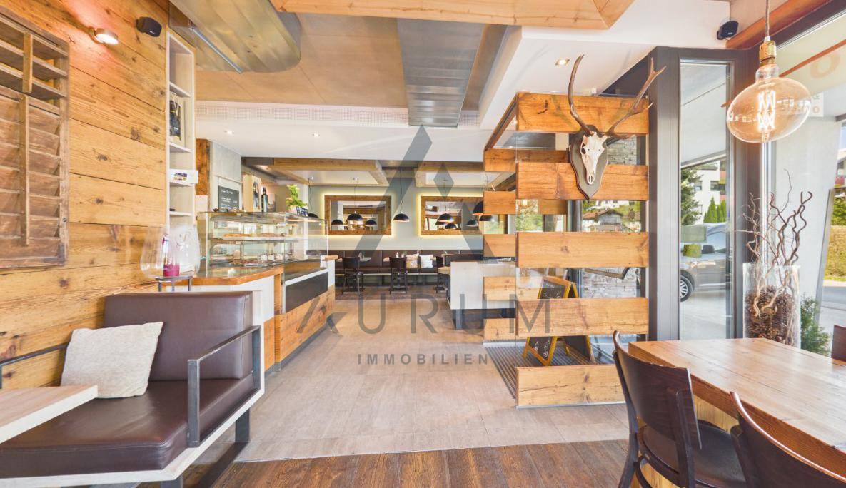 Innenansicht eines Cafés mit Holzwänden, einer Kuchentheke und rustikaler Dekoration, die eine gemütliche Atmosphäre schafft.