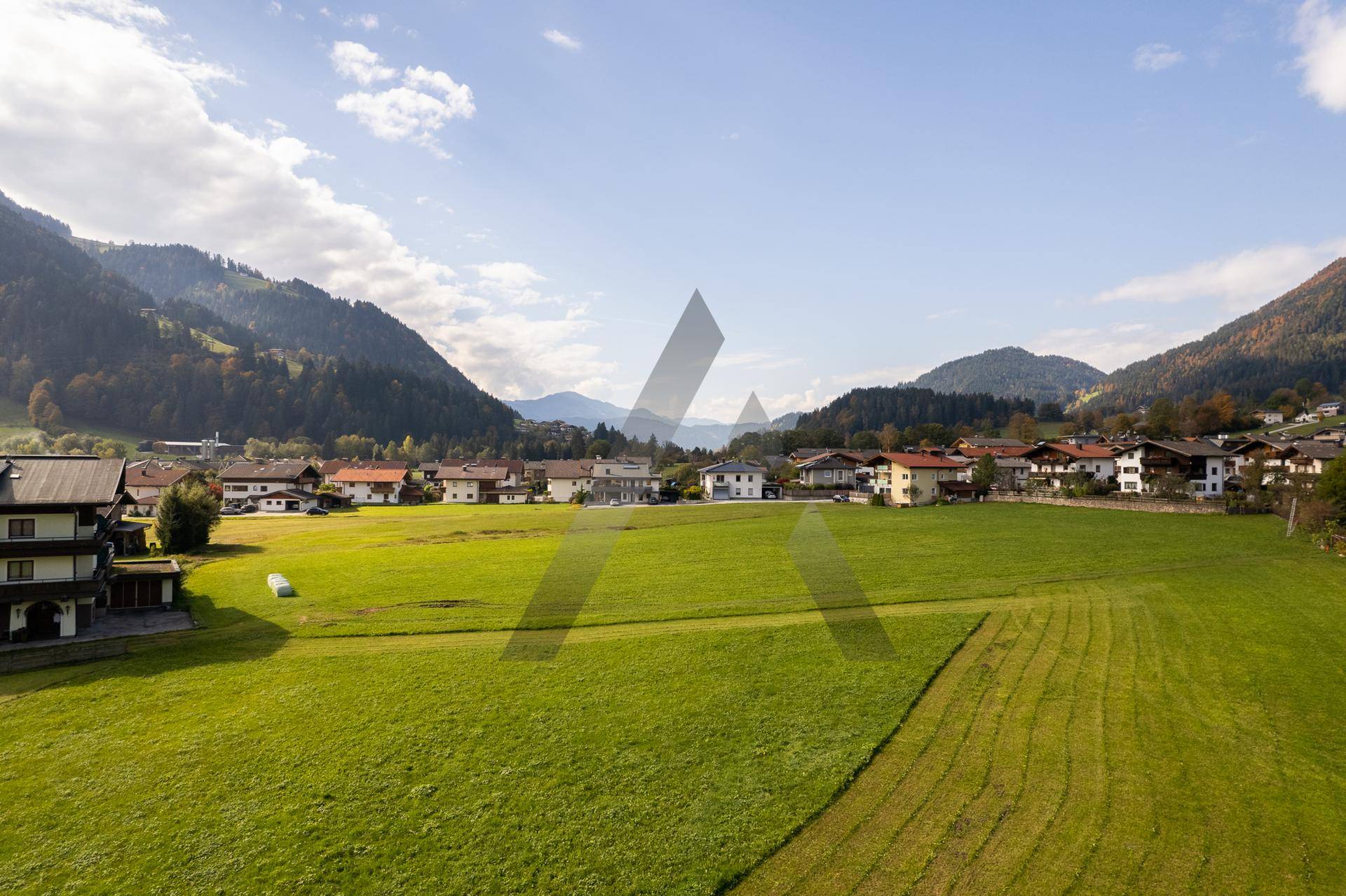Luftaufnahme eines charmanten Dorfes umgeben von weiten grünen Feldern und imposanten Bergen.