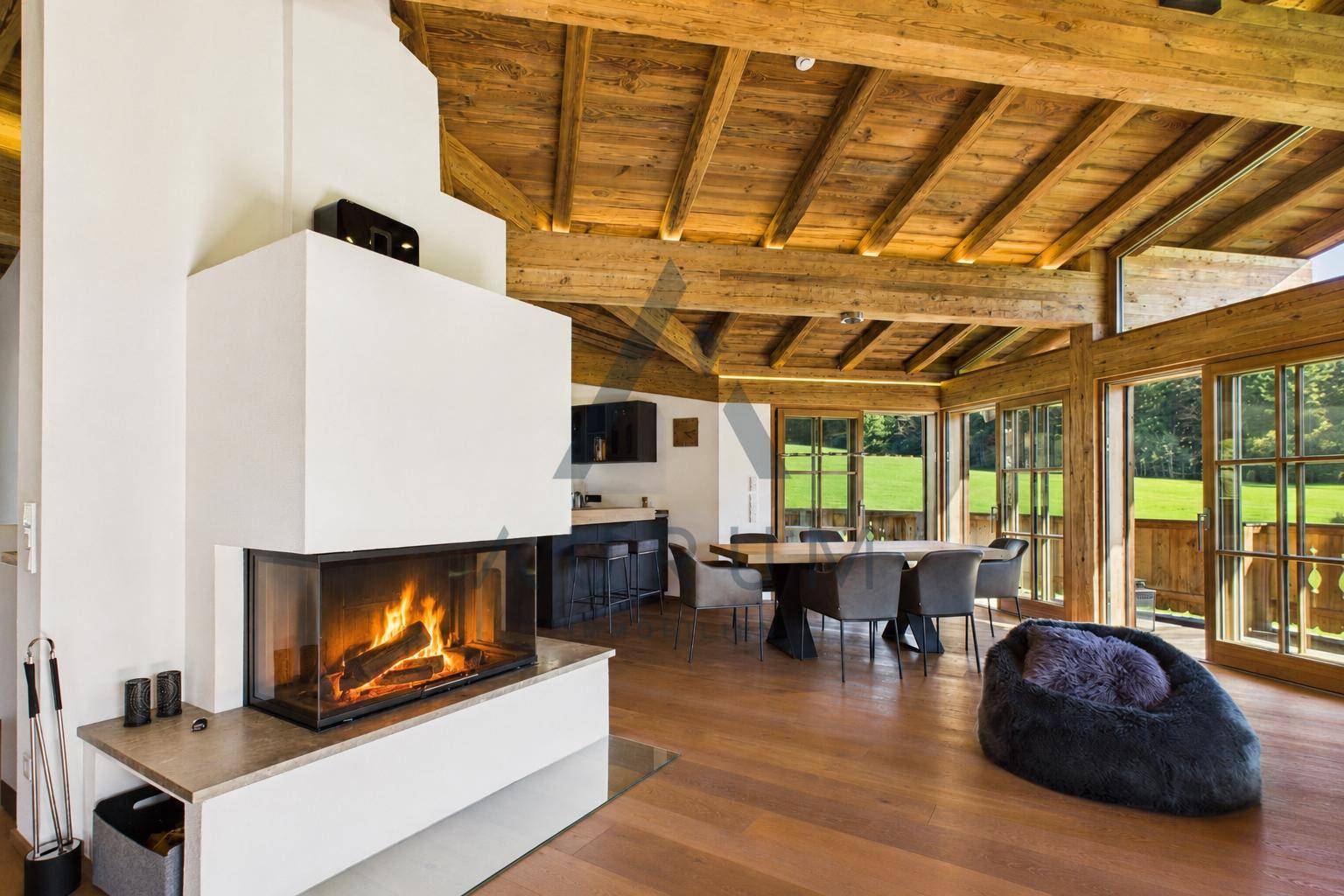 Offener Wohn-Essbereich mit Kamin, Holzbalkendecke und Zugang zu großen Fenstern.