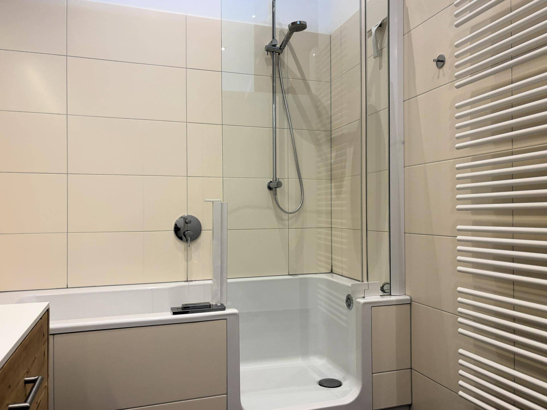 Helles Badezimmer mit Badewanne und integrierter Duschfunktion sowie einem Handtuchheizkörper.