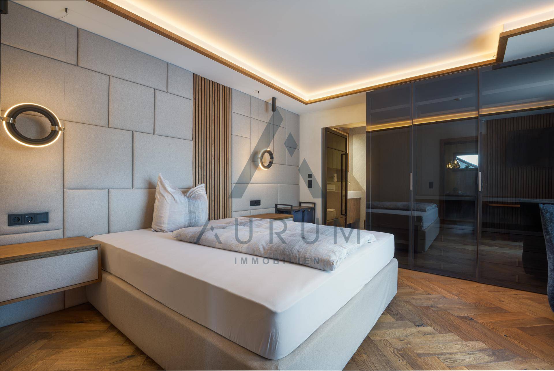 Elegantes Schlafzimmer mit gepolstertem Kopfteil, integrierten Schränken und indirekter Beleuchtung.