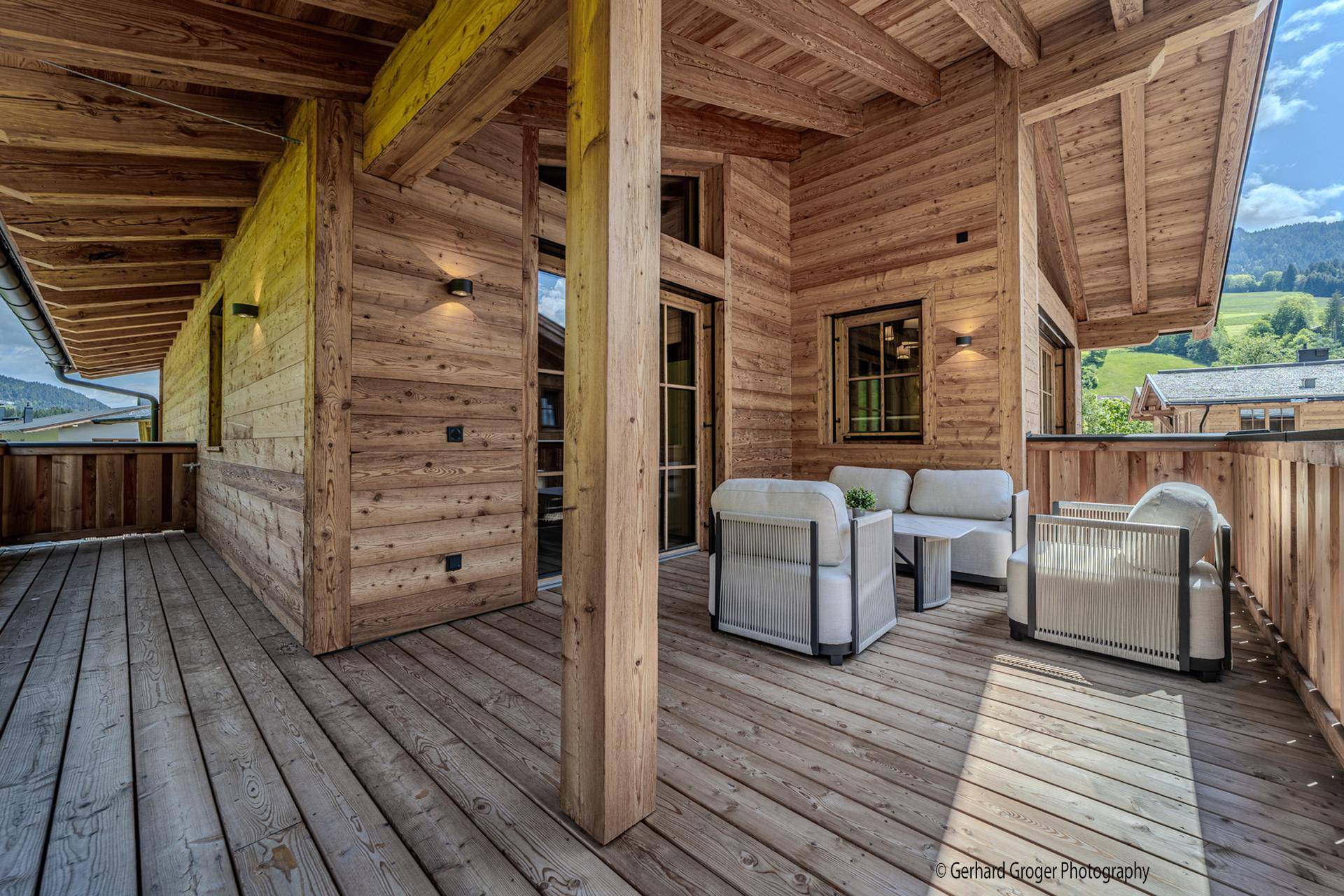Großer Holzbalkon mit bequemen Outdoor-Möbeln und Blick auf die grüne Berglandschaft.