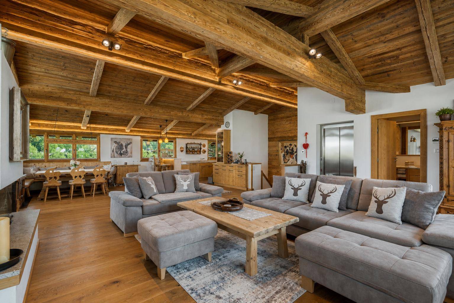 Heller Wohn- und Essbereich im Chalet-Stil mit Holzbalken, gemütlicher Sitzecke und integriertem Aufzug.