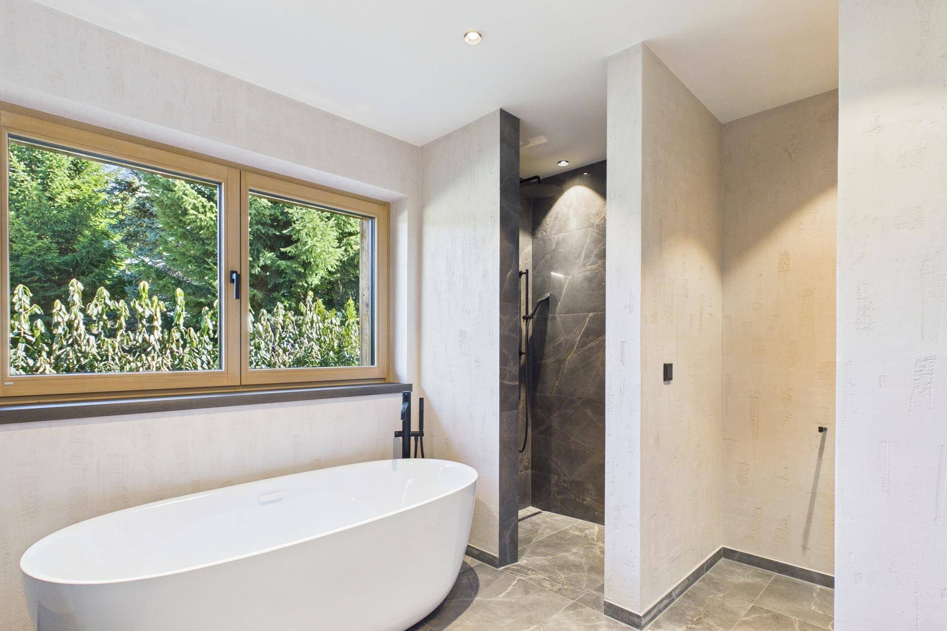 Helles Badezimmer mit freistehender Badewanne, Dusche und Fenster mit Grünblick.