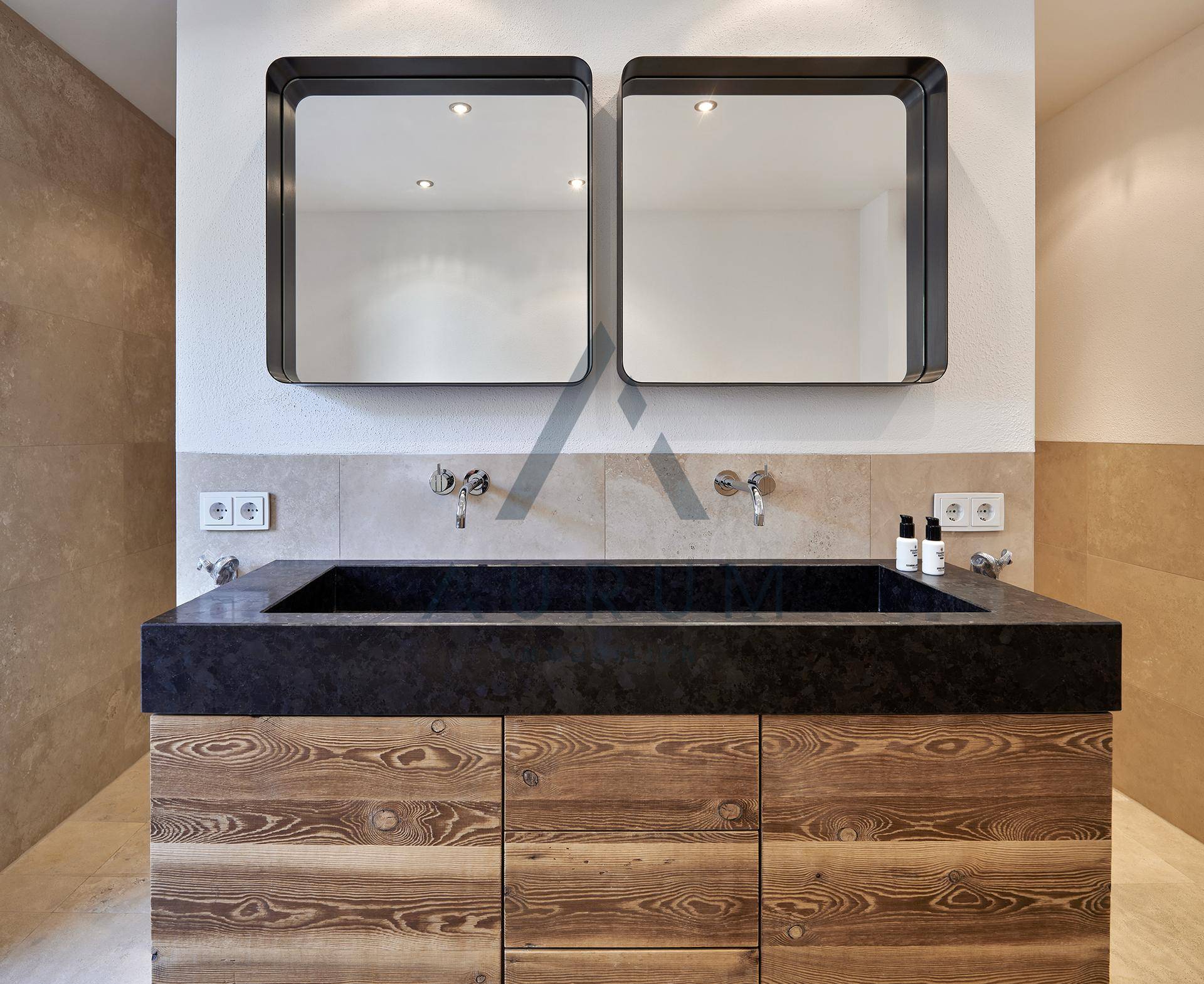 Modernes Badezimmer mit Doppelwaschbecken aus dunklem Stein und Holzunterschrank, hell gefliest.