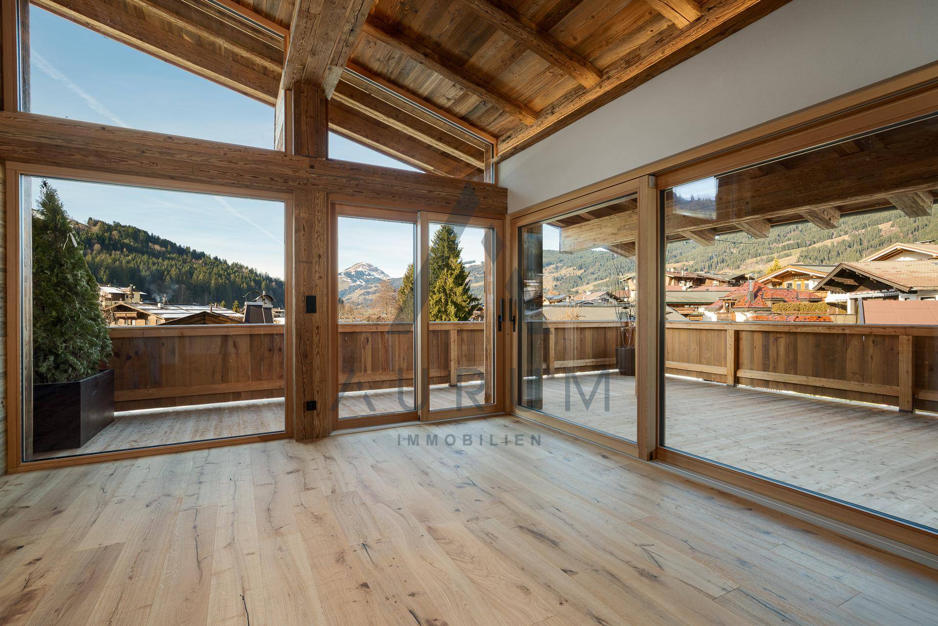 Heller Wohnbereich mit großen Glasfronten, Holzbalkendecke und weitem Blick auf die Berge.