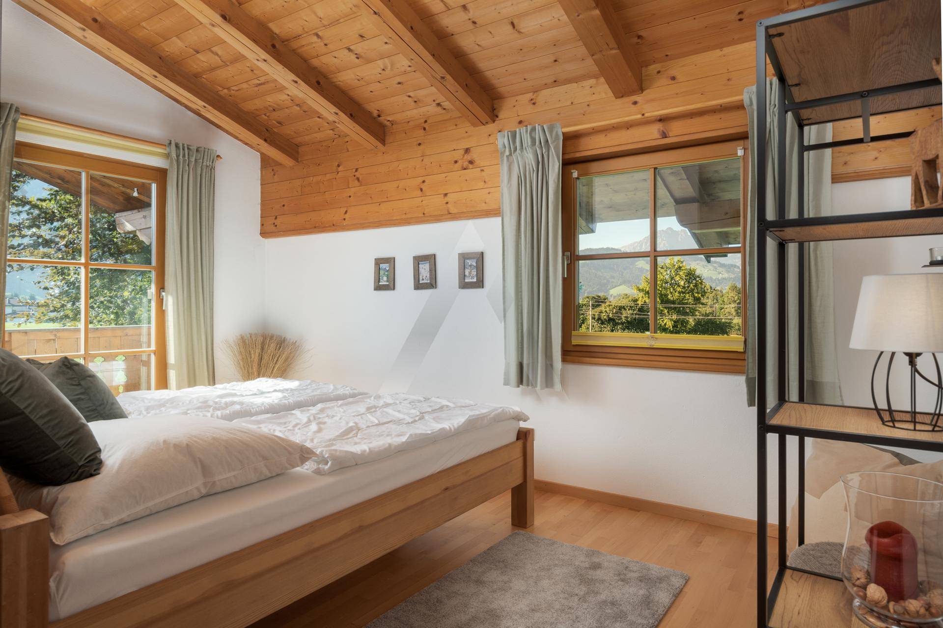 Helles Schlafzimmer mit Holzbalkendecke, Doppelbett und Fenstern mit Bergblick.