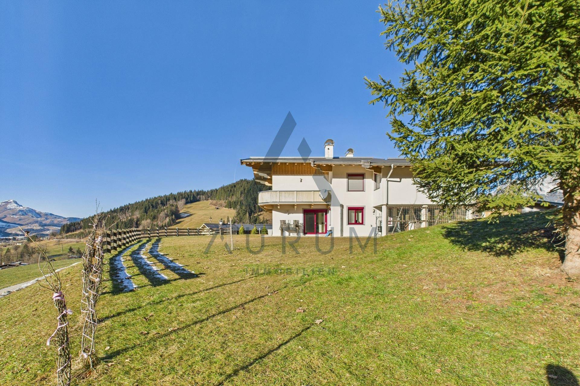 Haus in Hanglage mit weitem Blick auf die umliegende Berglandschaft und grüne Wiesen.