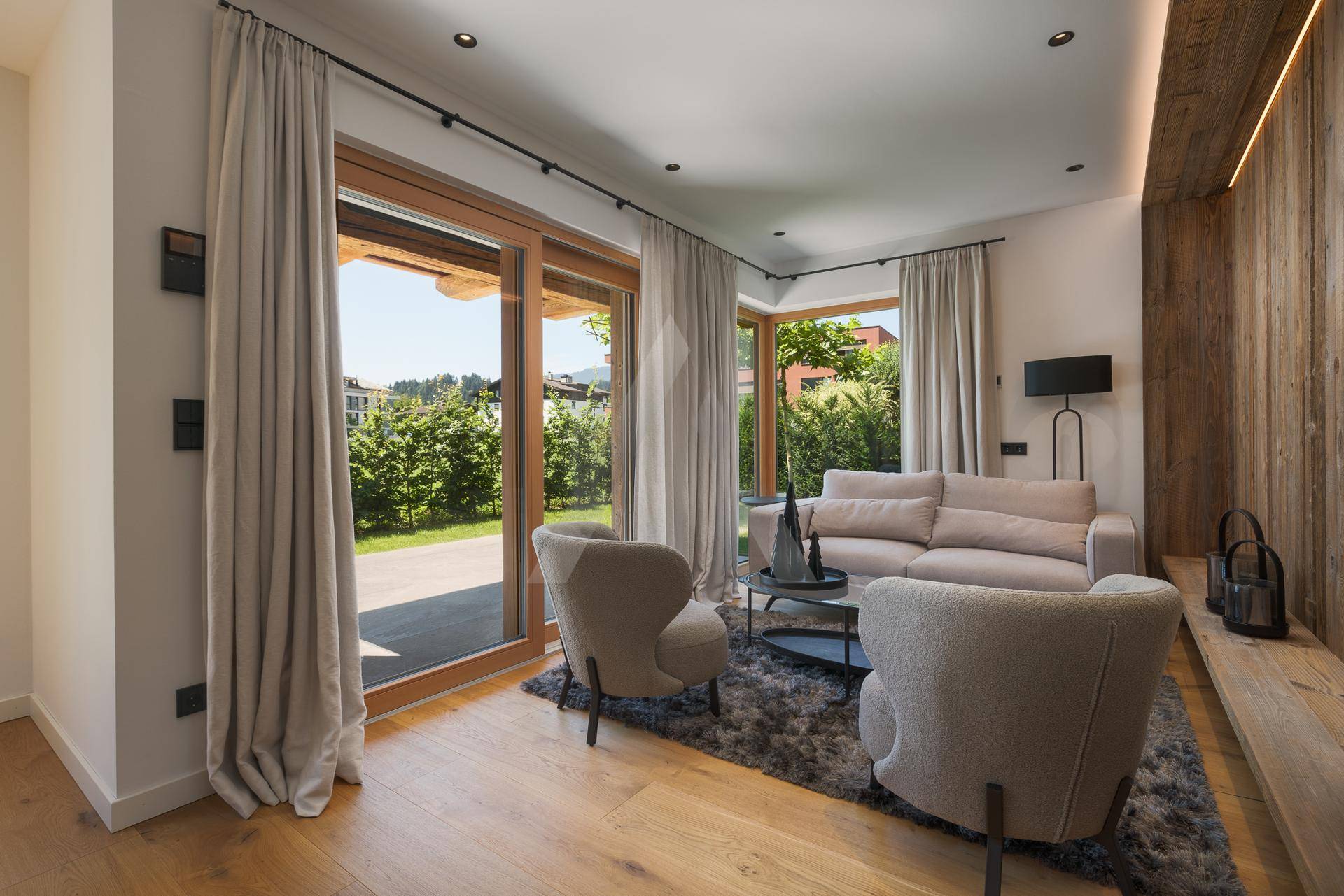 Gemütliches Wohnzimmer mit Holzboden, großen Fenstern und Zugang zum Garten.