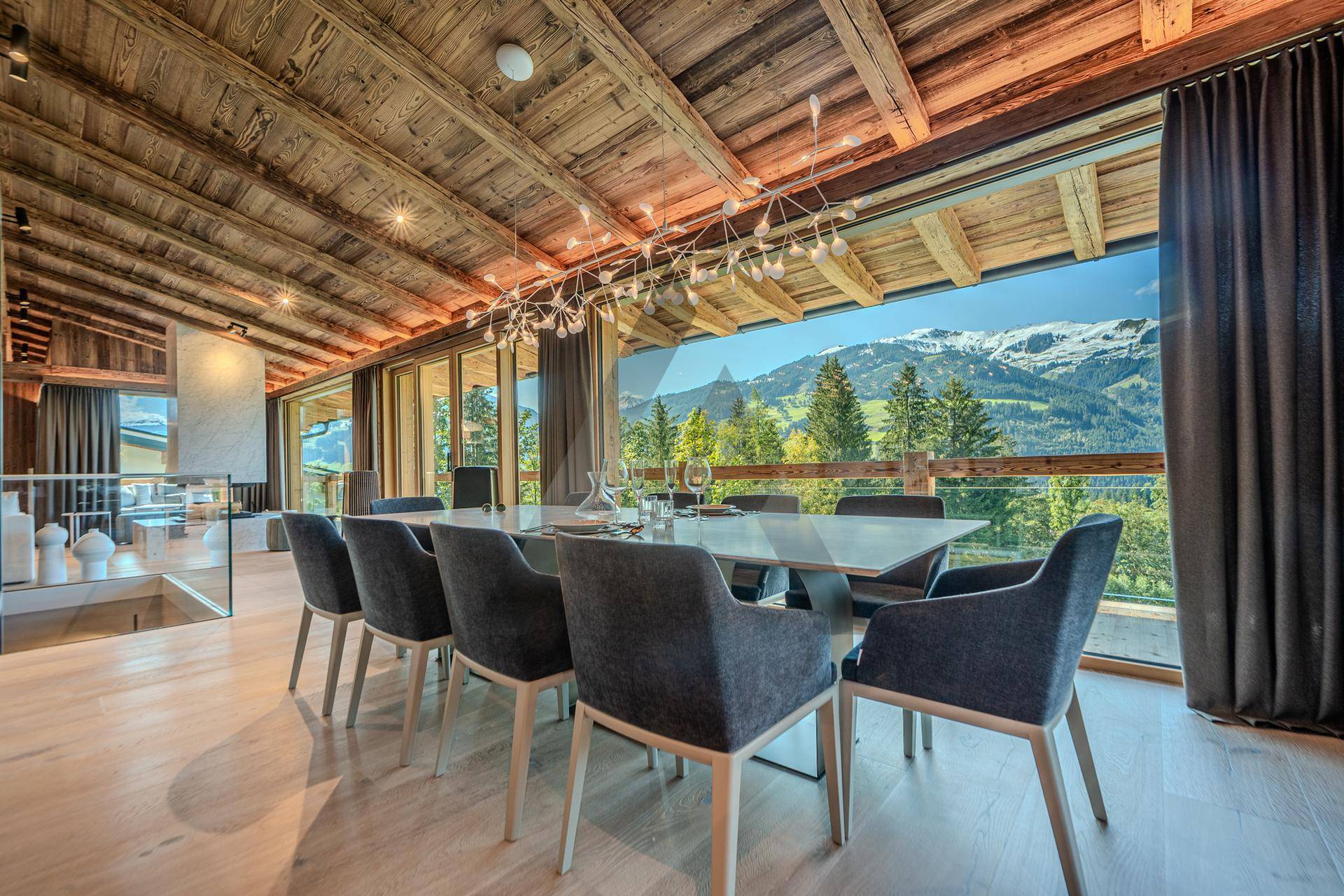 Eleganter Essbereich mit Holzbalkendecke, modernem Kronleuchter und Panoramafenstern mit Bergblick.